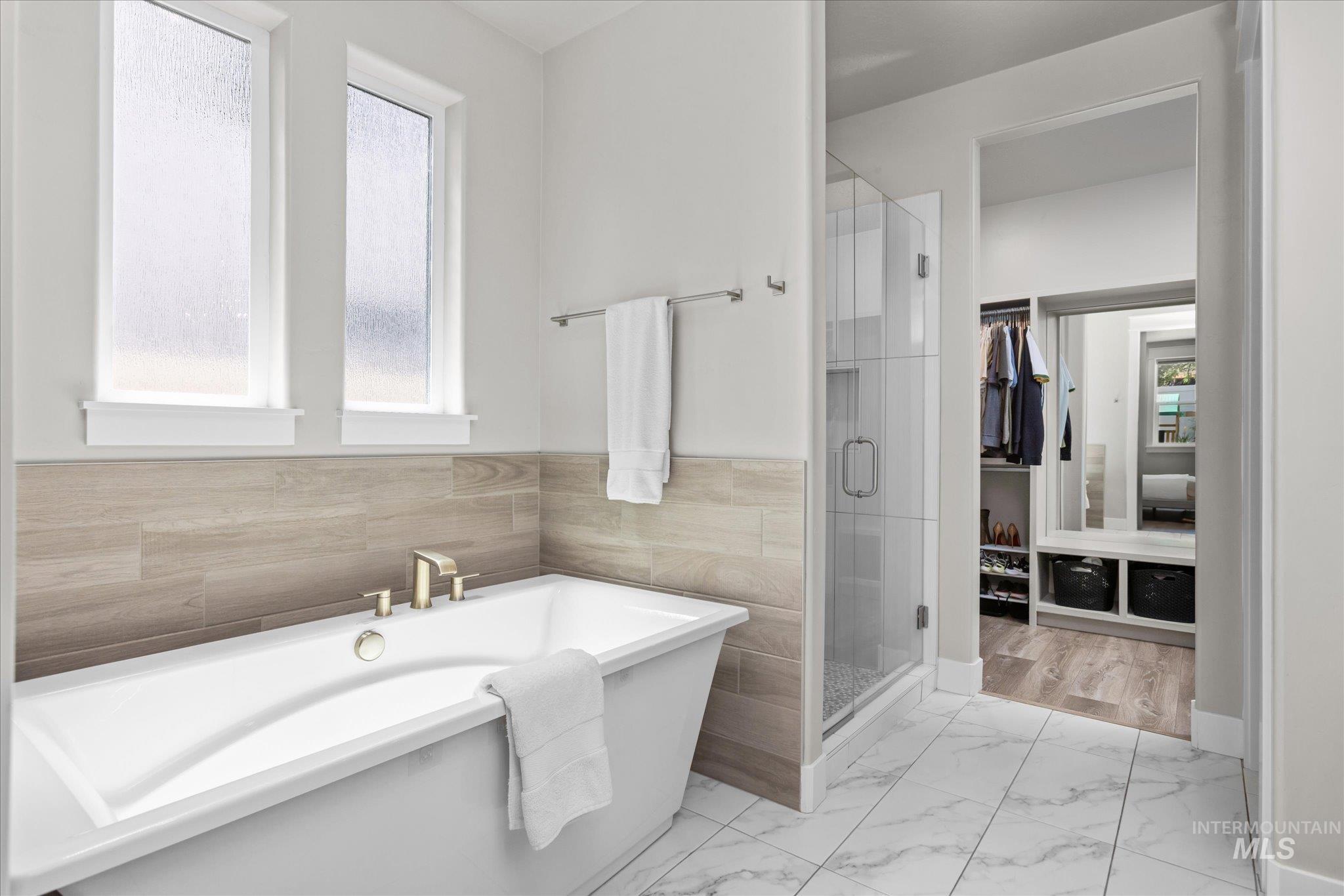 Bathroom with a freestanding bath, a shower stall, marble finish flooring, and tile walls