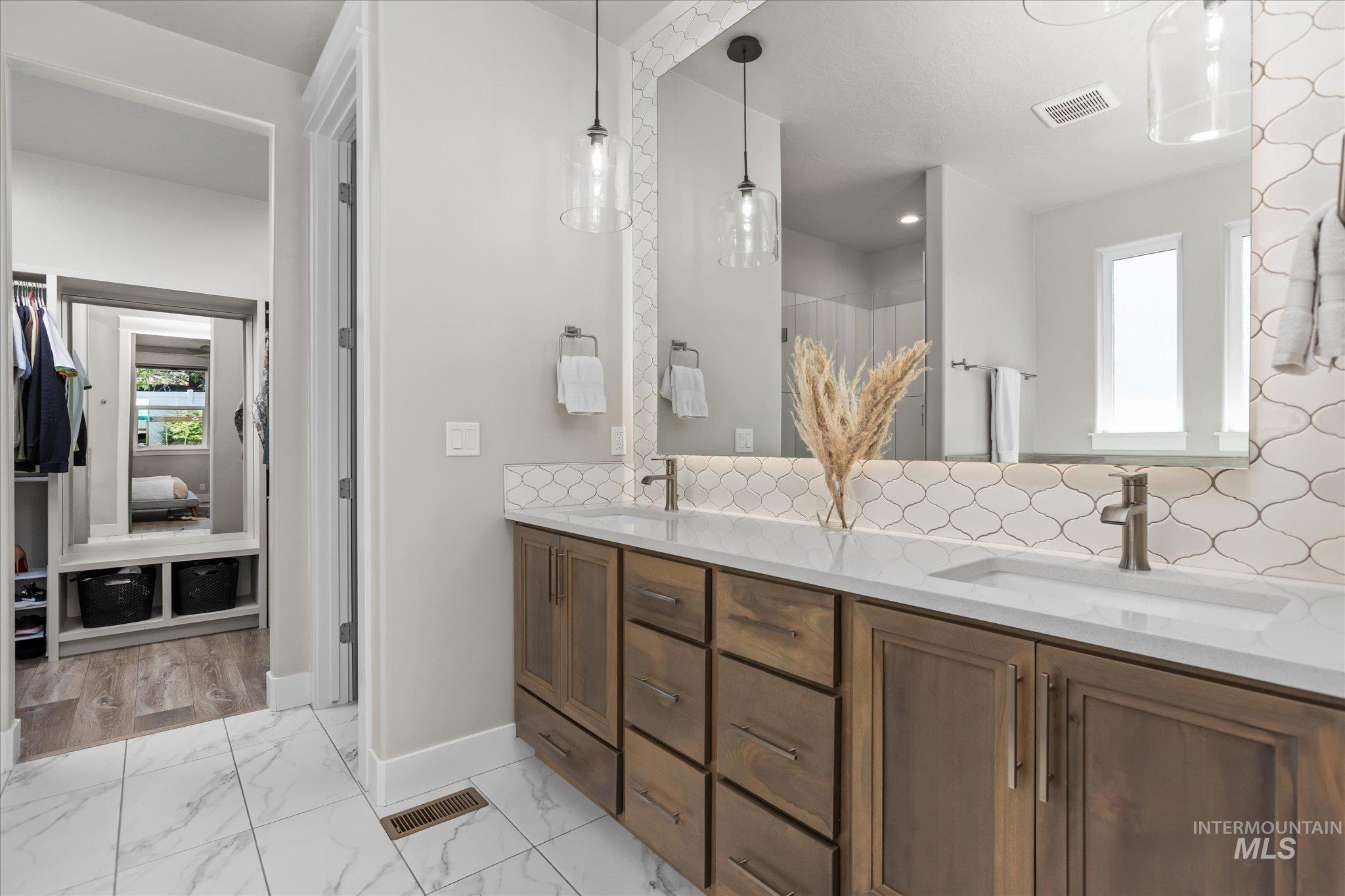 Bathroom with backsplash, double vanity, and marble look tiles