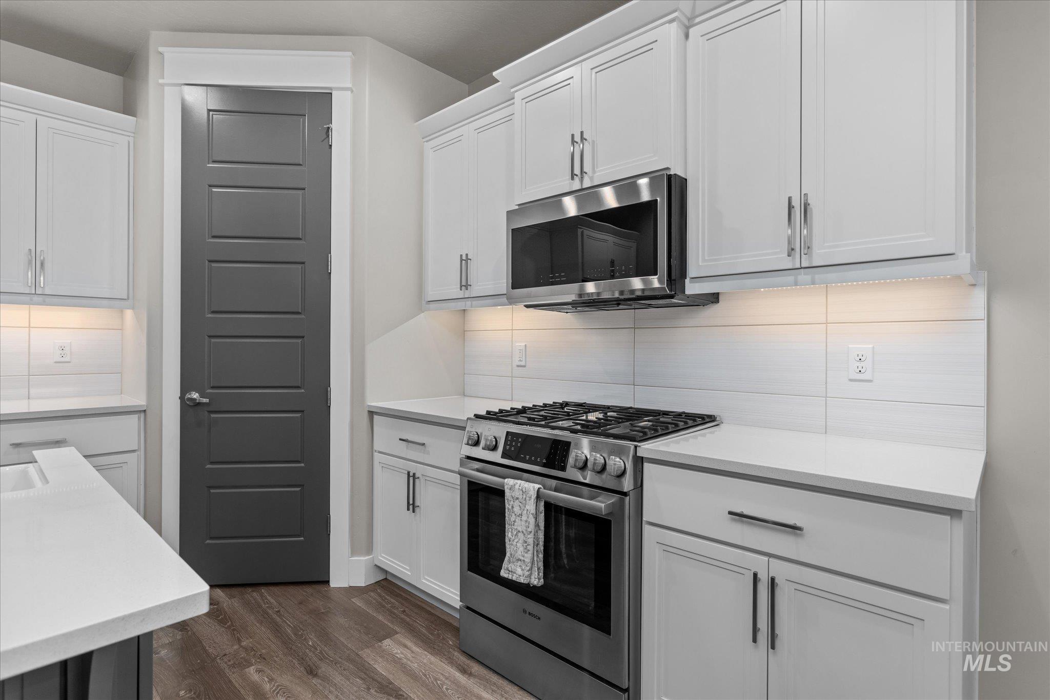 Kitchen featuring stainless steel appliances, decorative backsplash, dark wood-style flooring, and light countertops