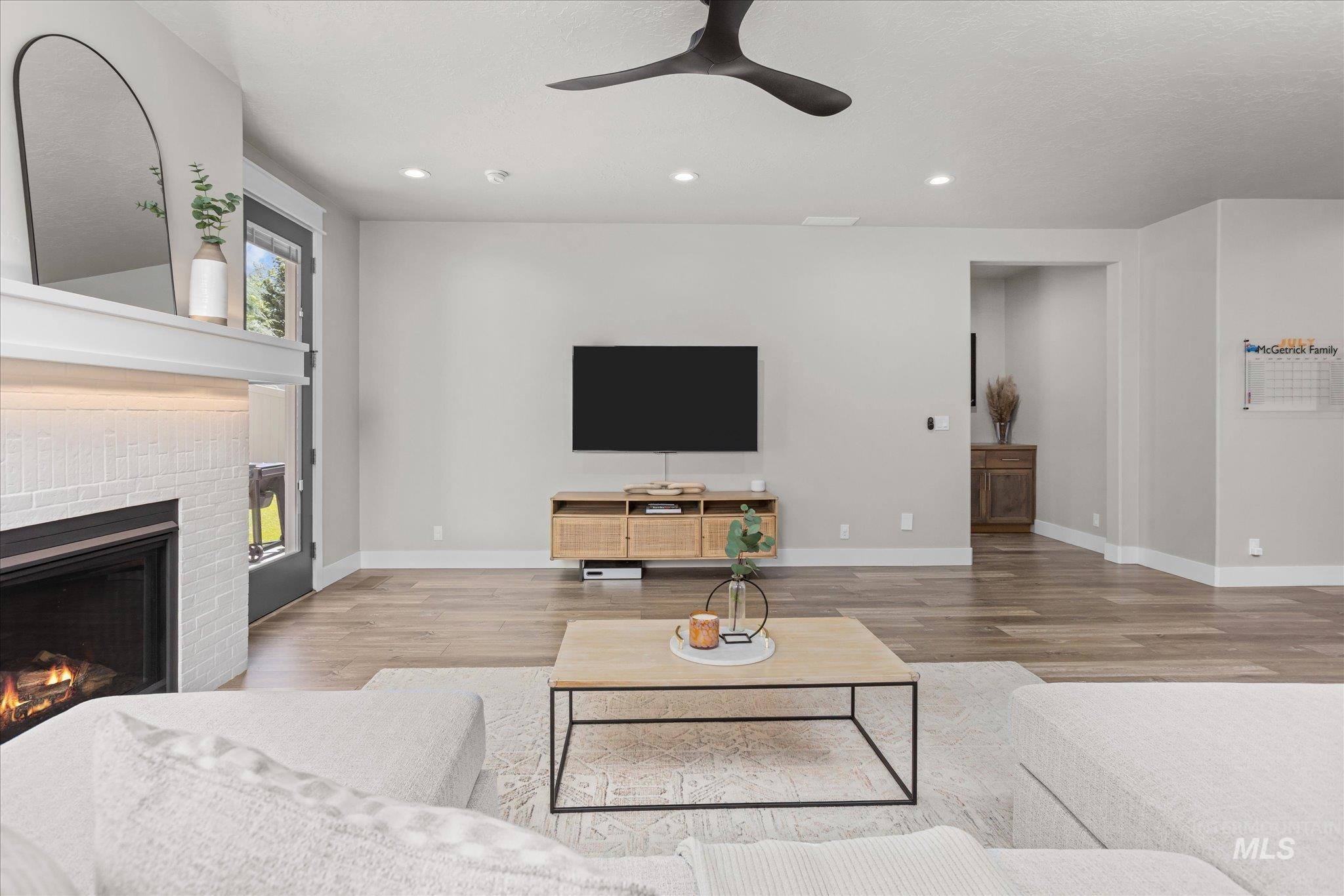 Living area featuring a brick fireplace, wood finished floors, a ceiling fan, and recessed lighting