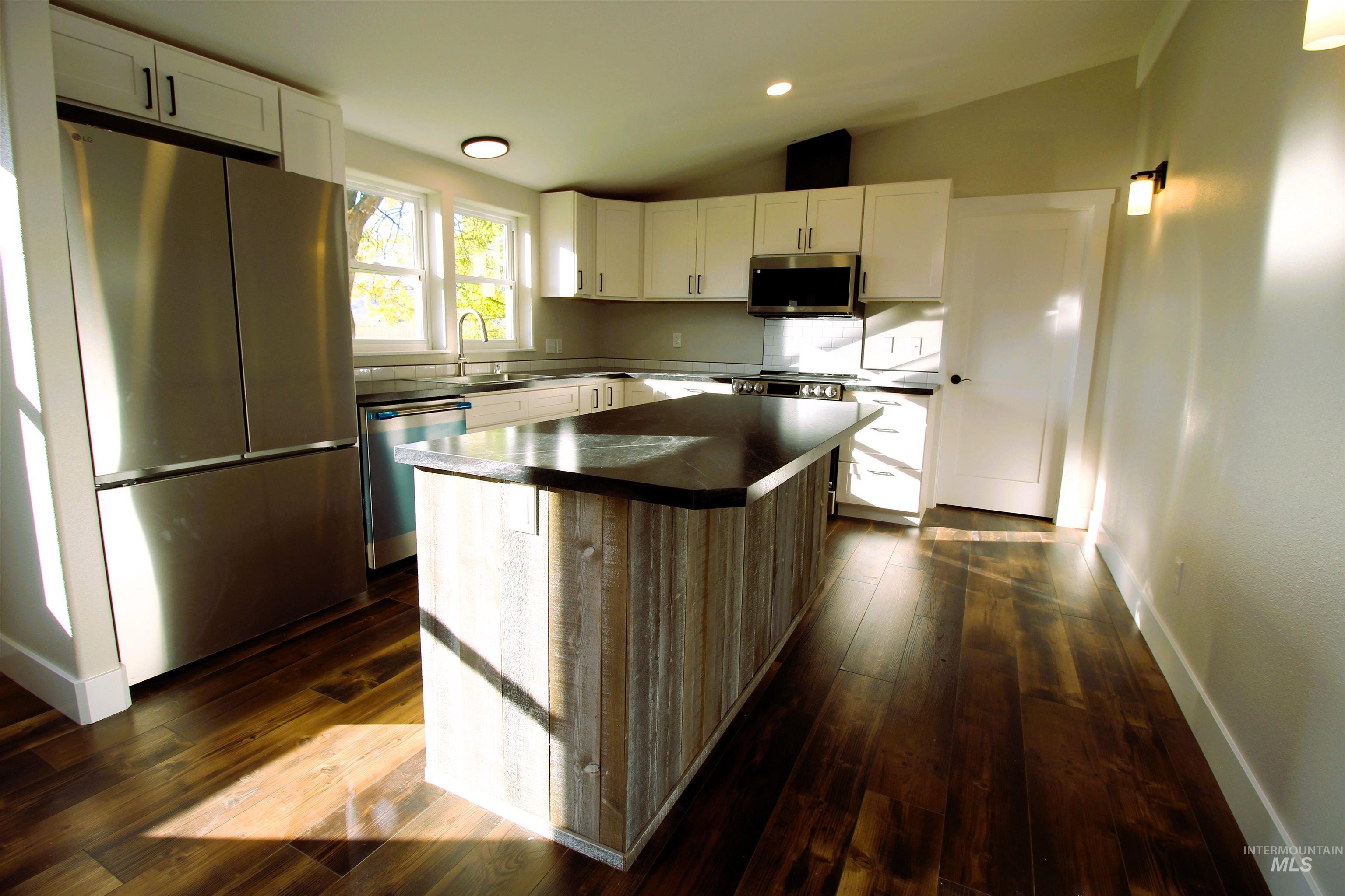 Kitchen with stainless steel appliances, a kitchen island, lofted ceiling, white cabinetry, and dark wood-style flooring