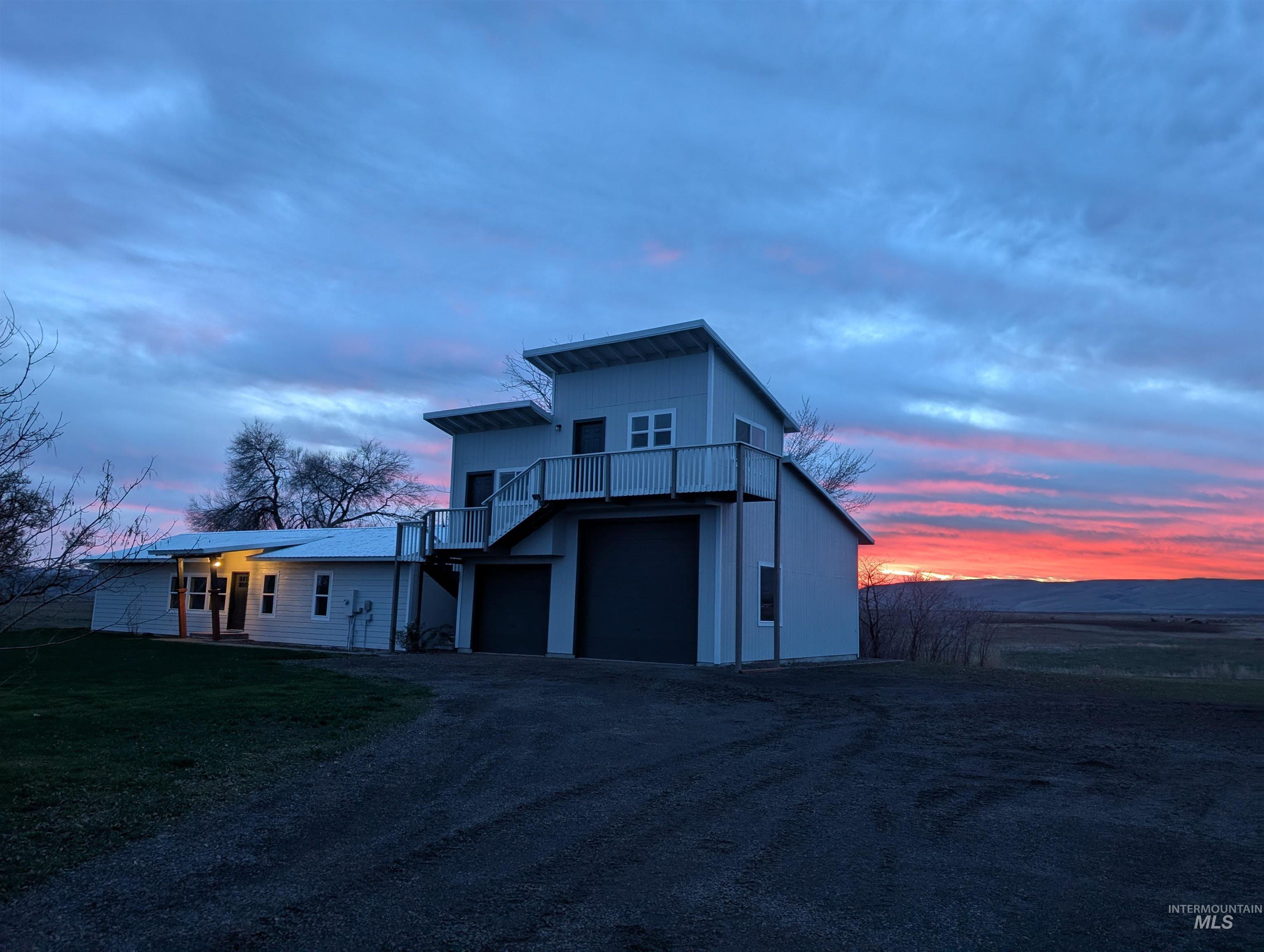 View of front of home featuring a balcony, dirt driveway, an attached garage, and a front yard