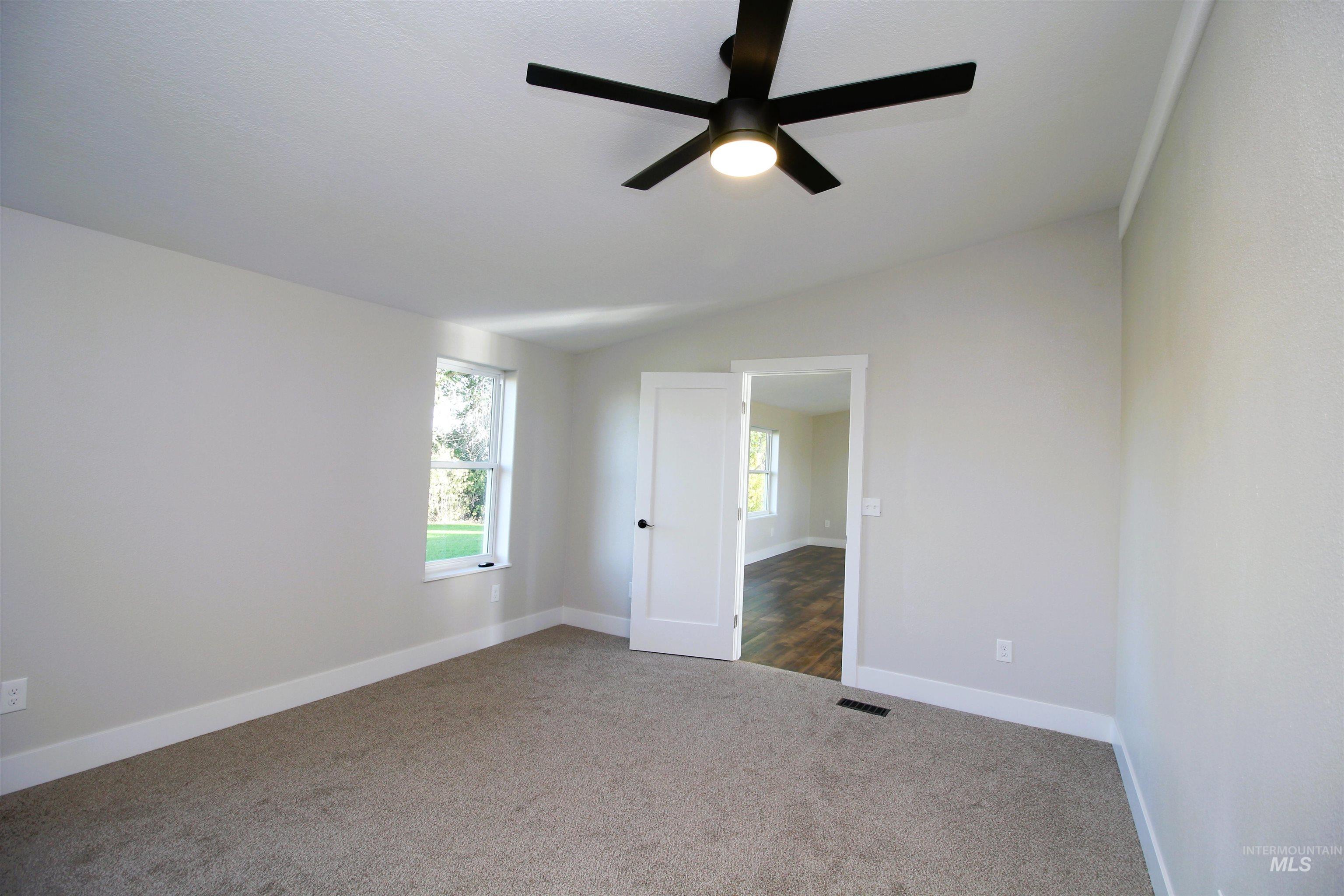 Unfurnished room with vaulted ceiling, dark colored carpet, and ceiling fan