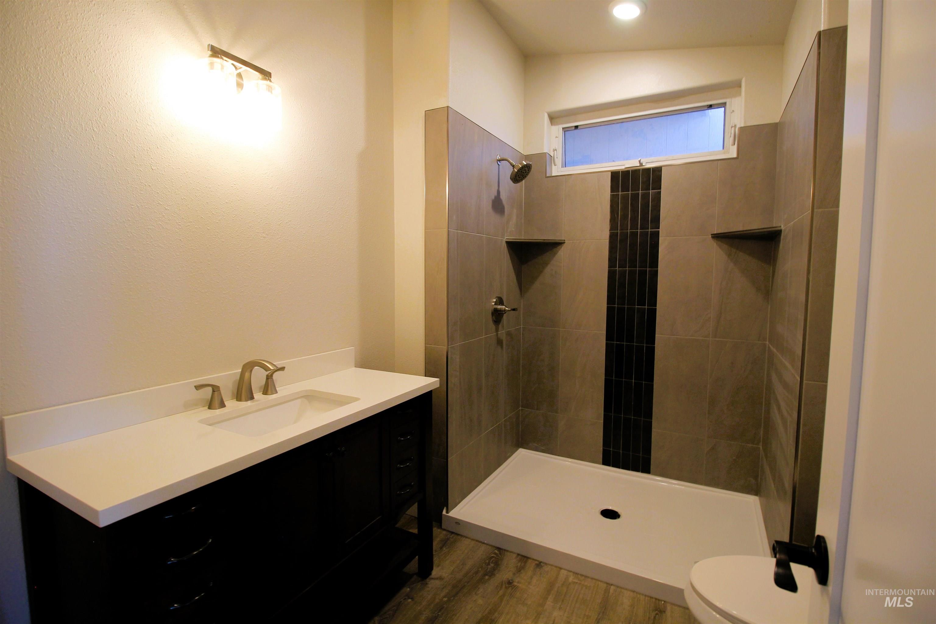 Full bathroom featuring vanity, dark wood finished floors, and tiled shower