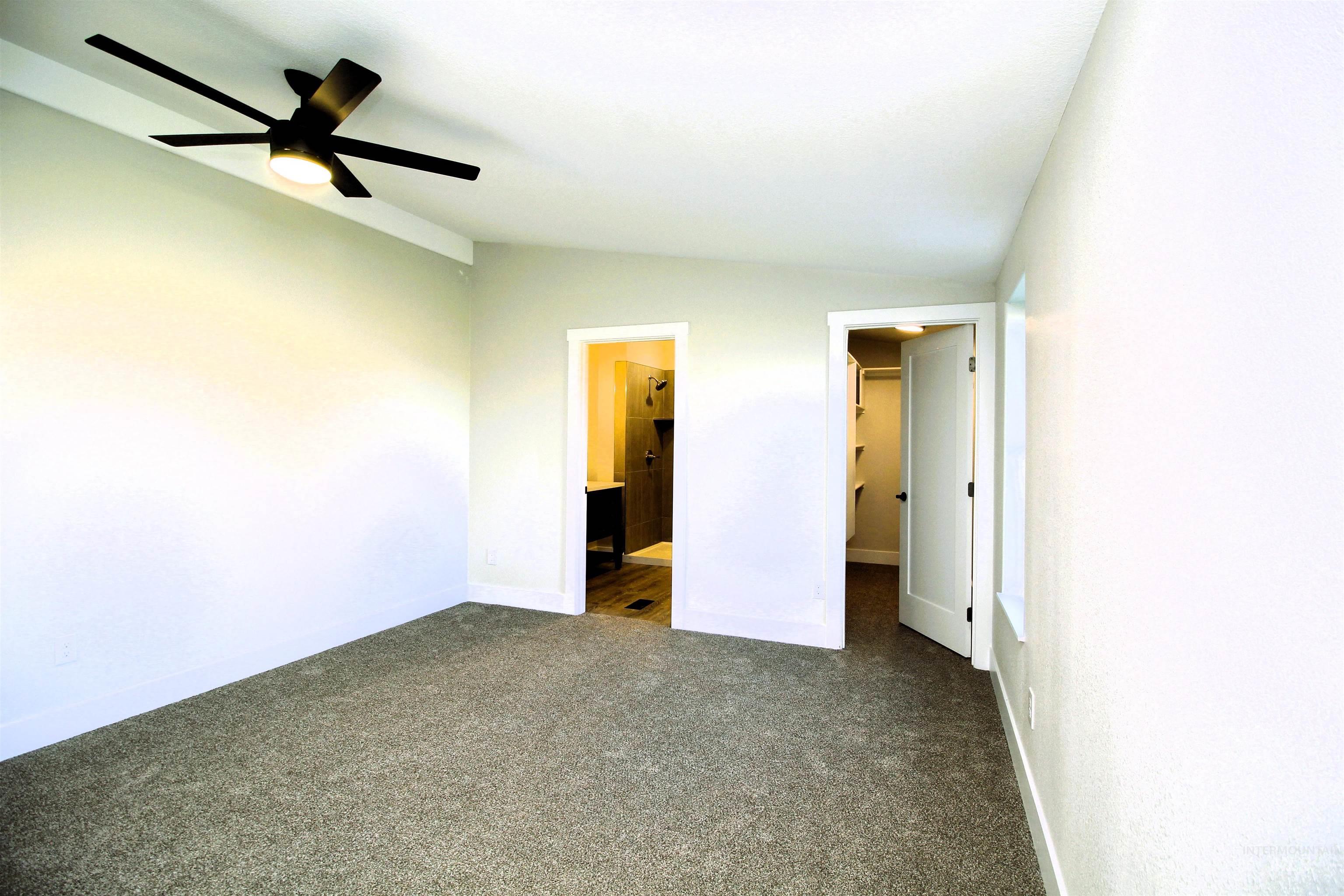 Unfurnished bedroom with a spacious closet, carpet floors, ceiling fan, ensuite bath, and vaulted ceiling