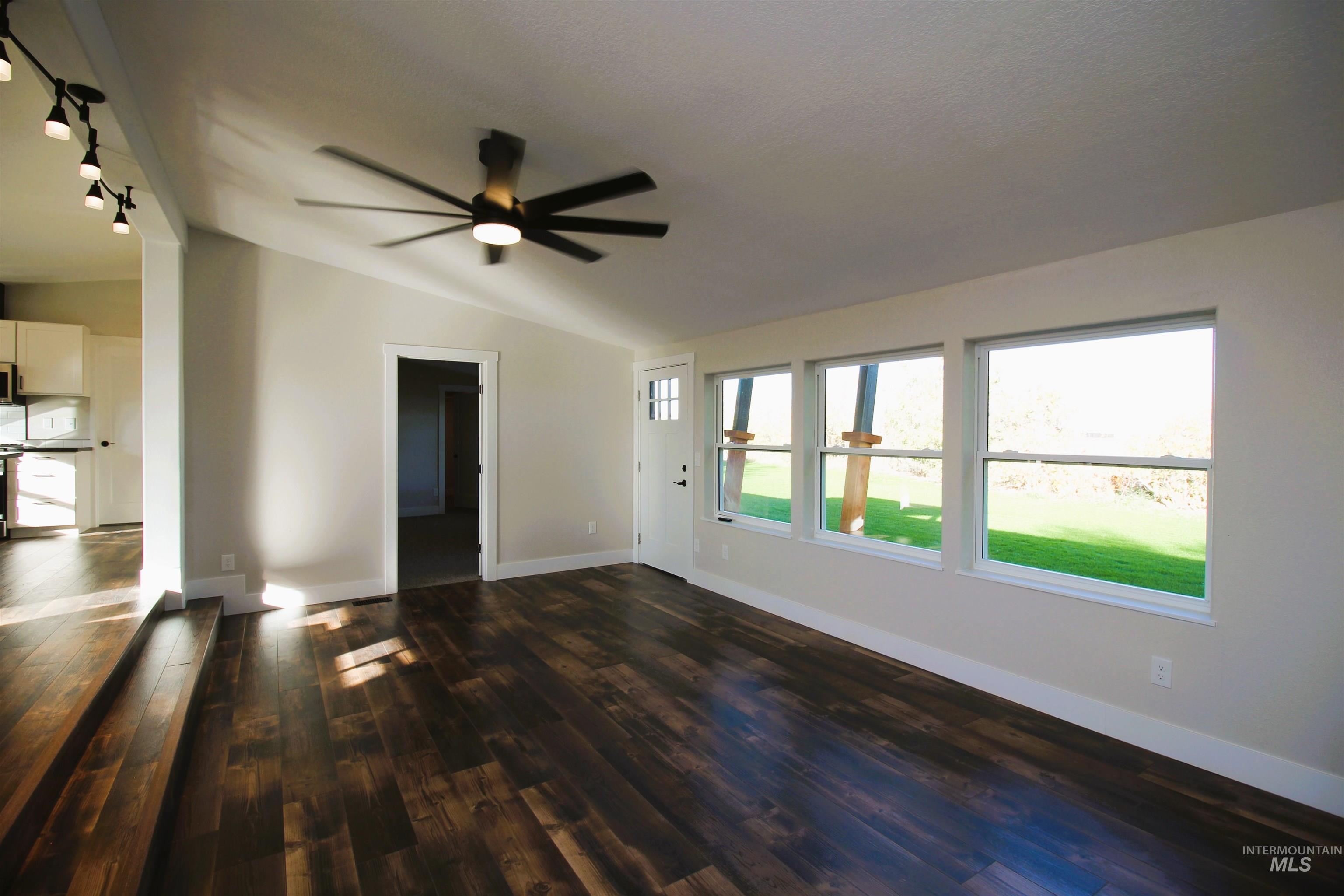 Unfurnished living room featuring vaulted ceiling, dark wood-type flooring, and a ceiling fan