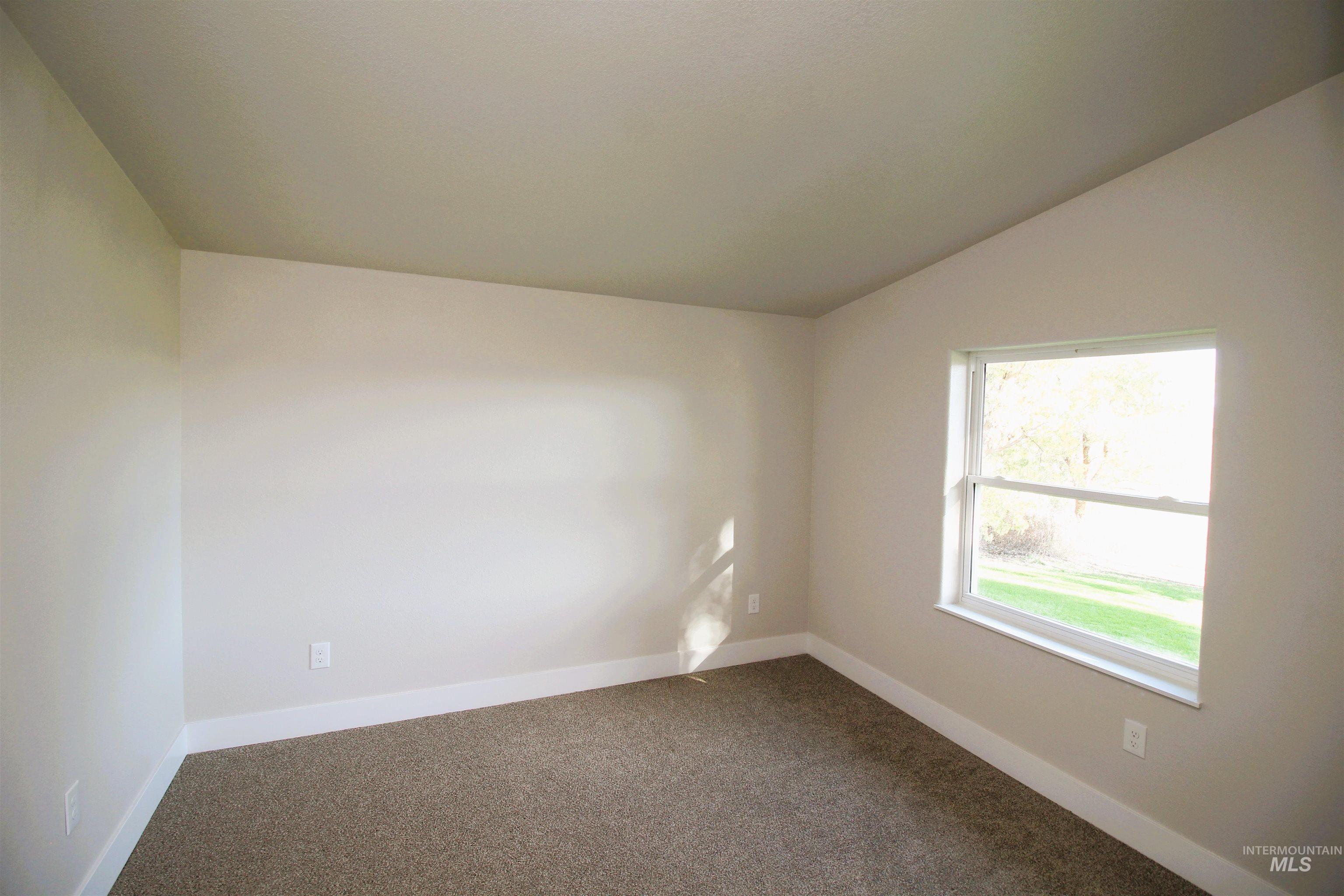 Carpeted spare room featuring baseboards and lofted ceiling