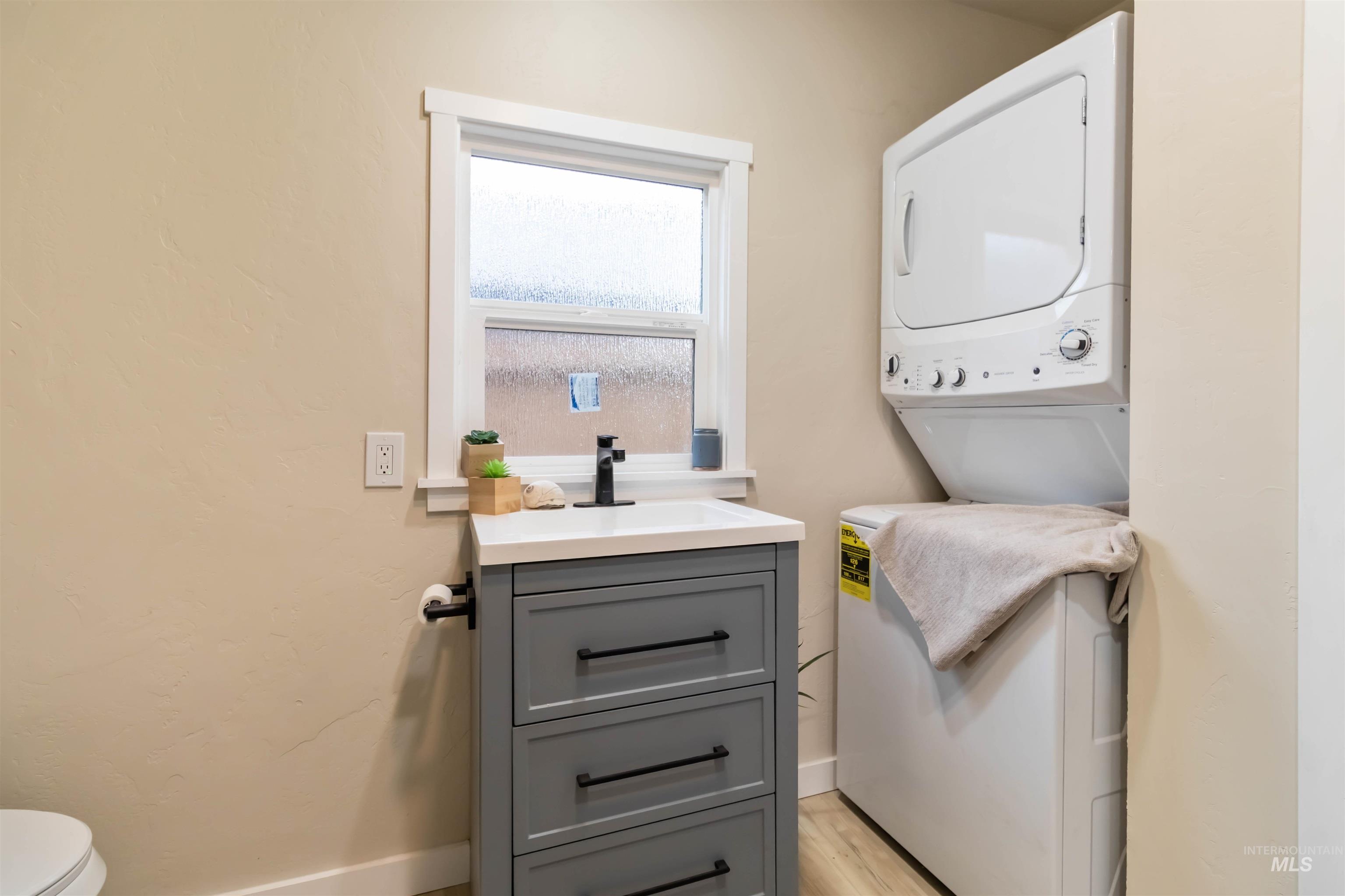 Laundry area with stacked washer / dryer and light wood finished floors