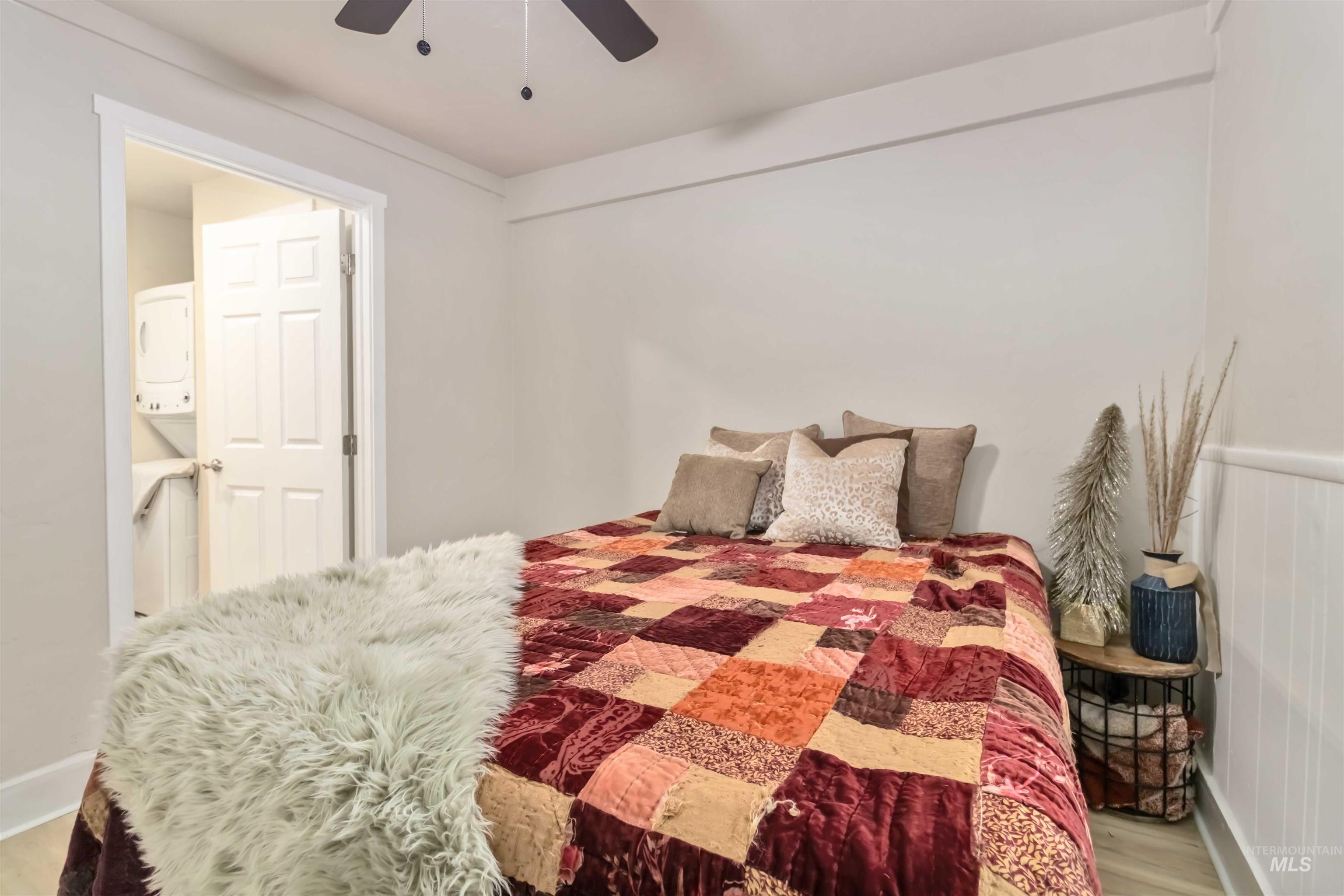 Bedroom with light wood-type flooring, stacked washer / drying machine, and ceiling fan