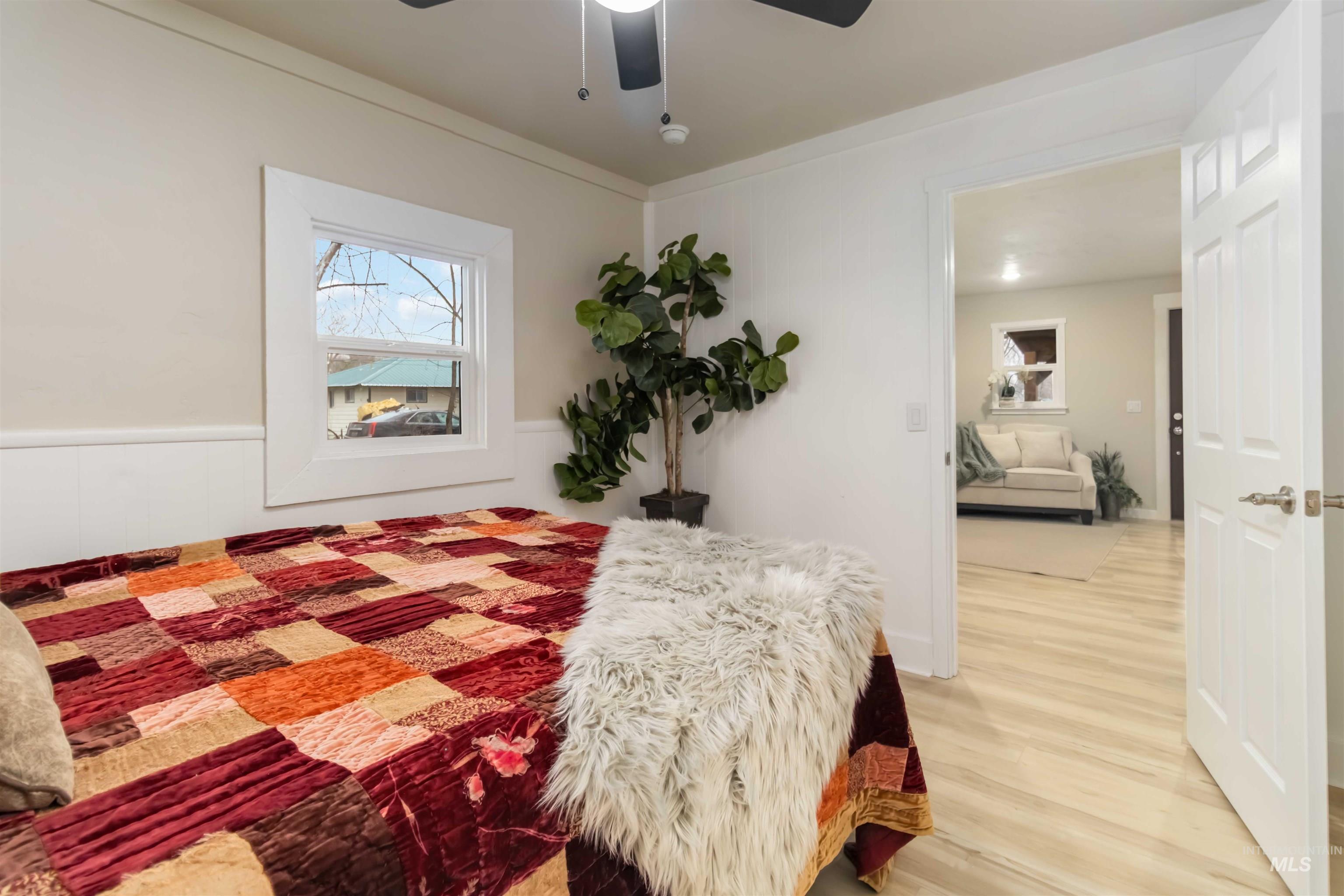 Bedroom featuring light wood finished floors, a ceiling fan, and a wainscoted wall
