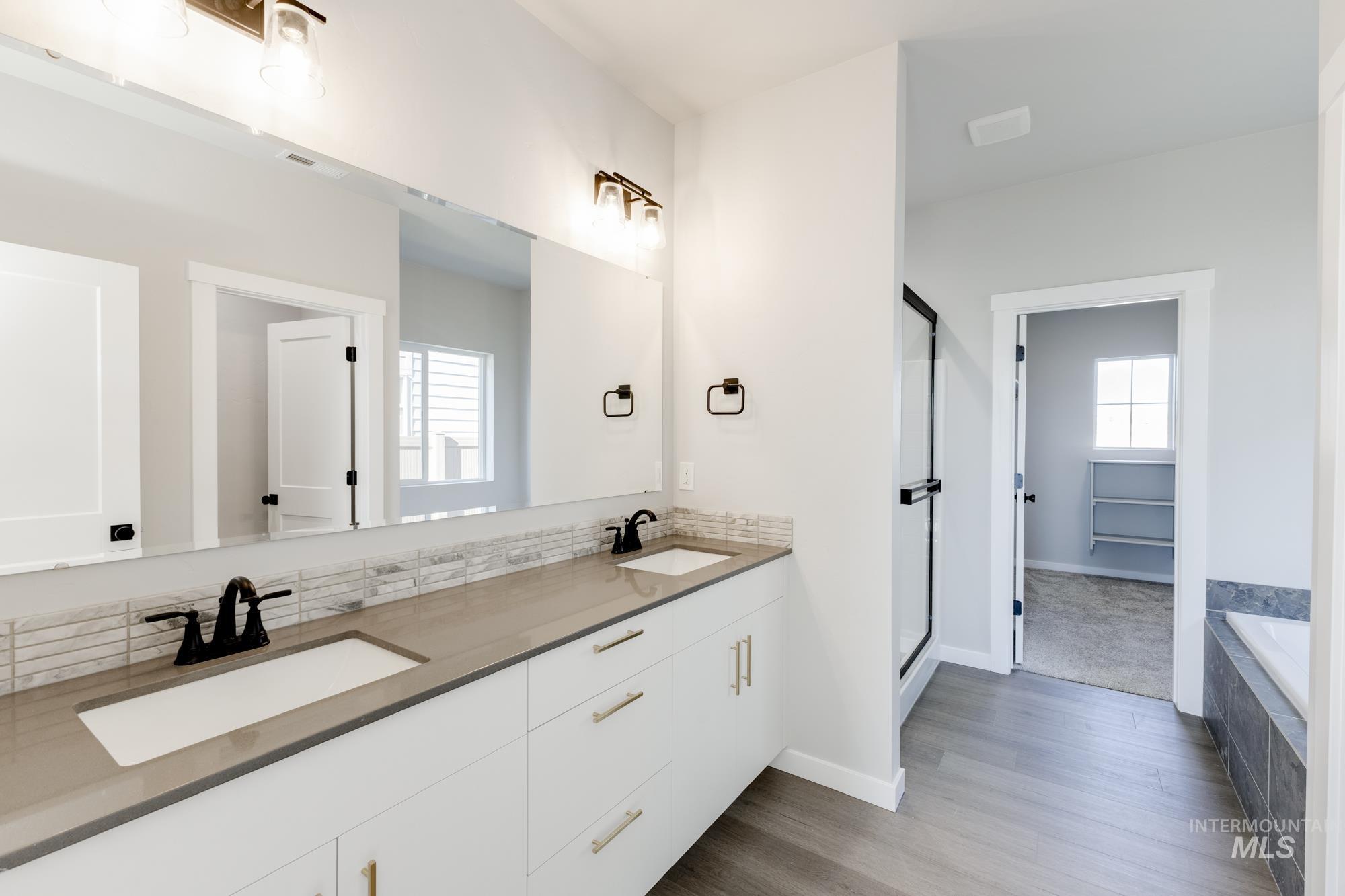 Full bathroom with double vanity, tiled bath, a stall shower, and dark wood-type flooring