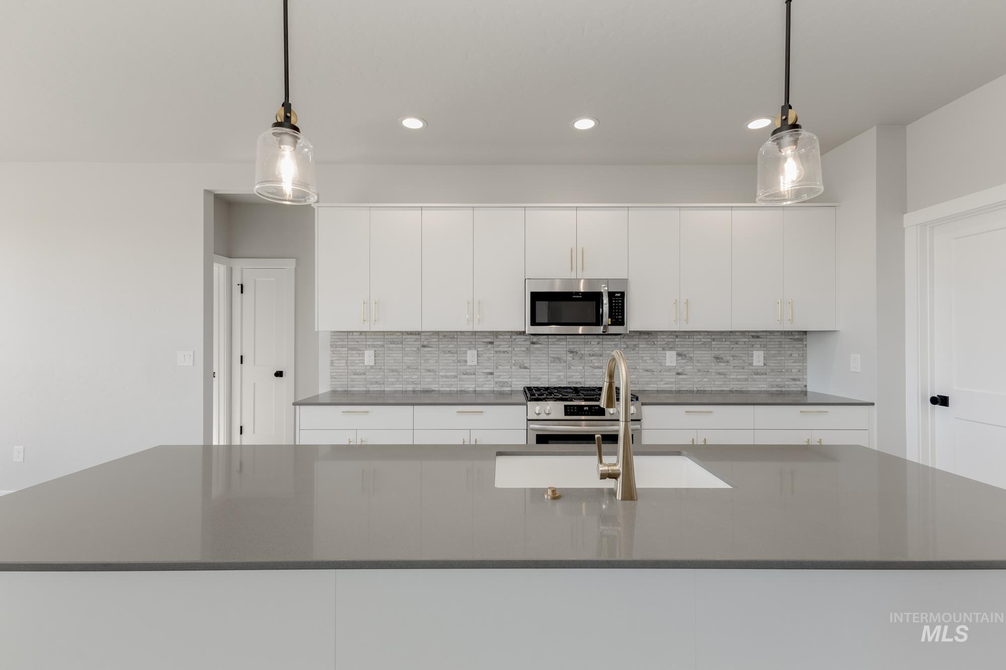 Kitchen with white cabinets, appliances with stainless steel finishes, hanging light fixtures, decorative backsplash, and recessed lighting
