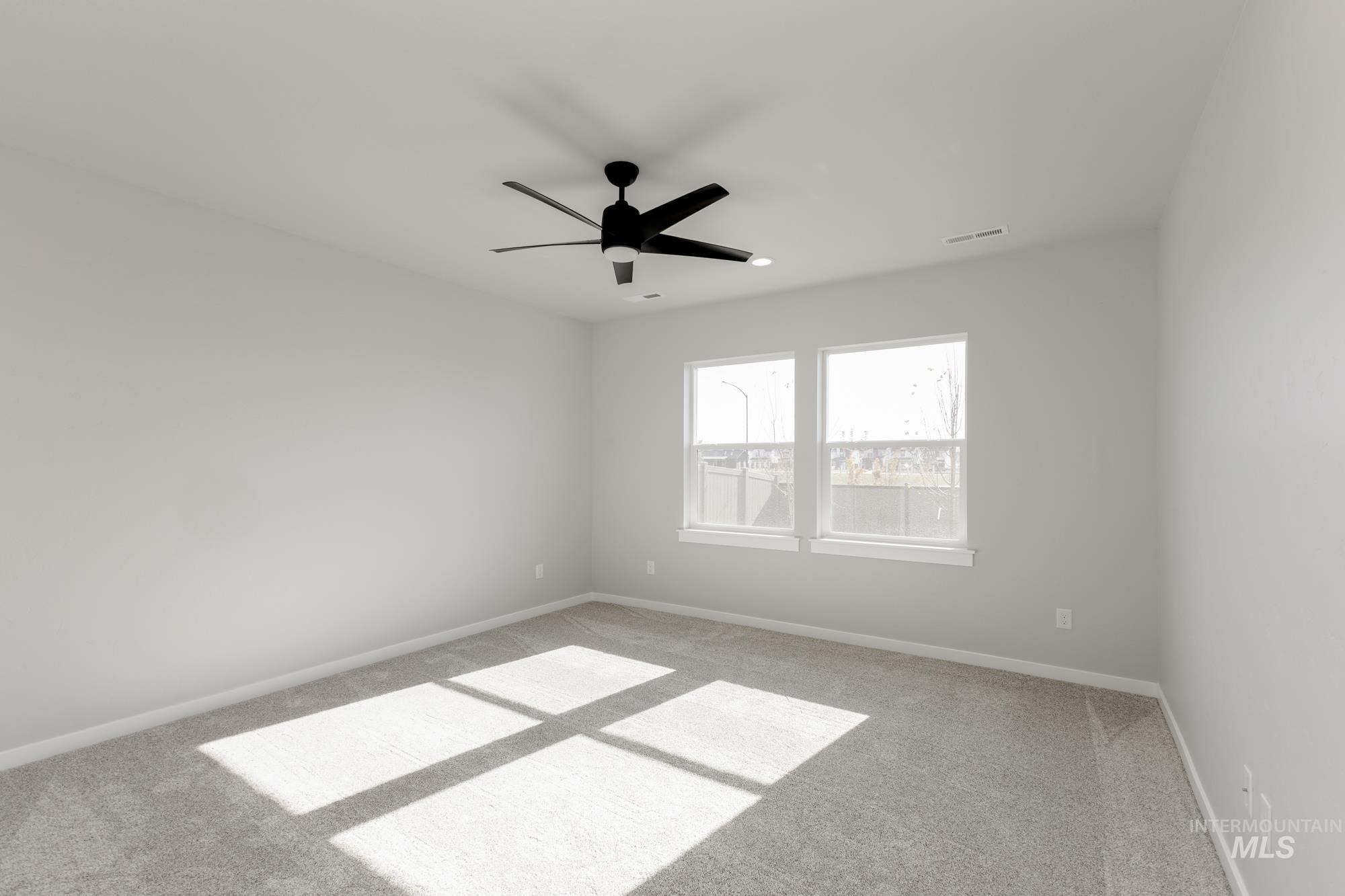 Carpeted spare room featuring a ceiling fan and baseboards