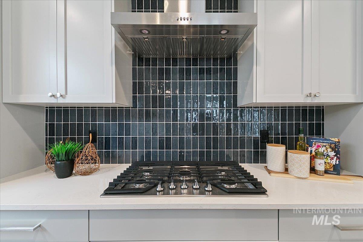 Kitchen featuring wall chimney range hood, white cabinets, decorative backsplash, stainless steel gas cooktop, and light stone countertops