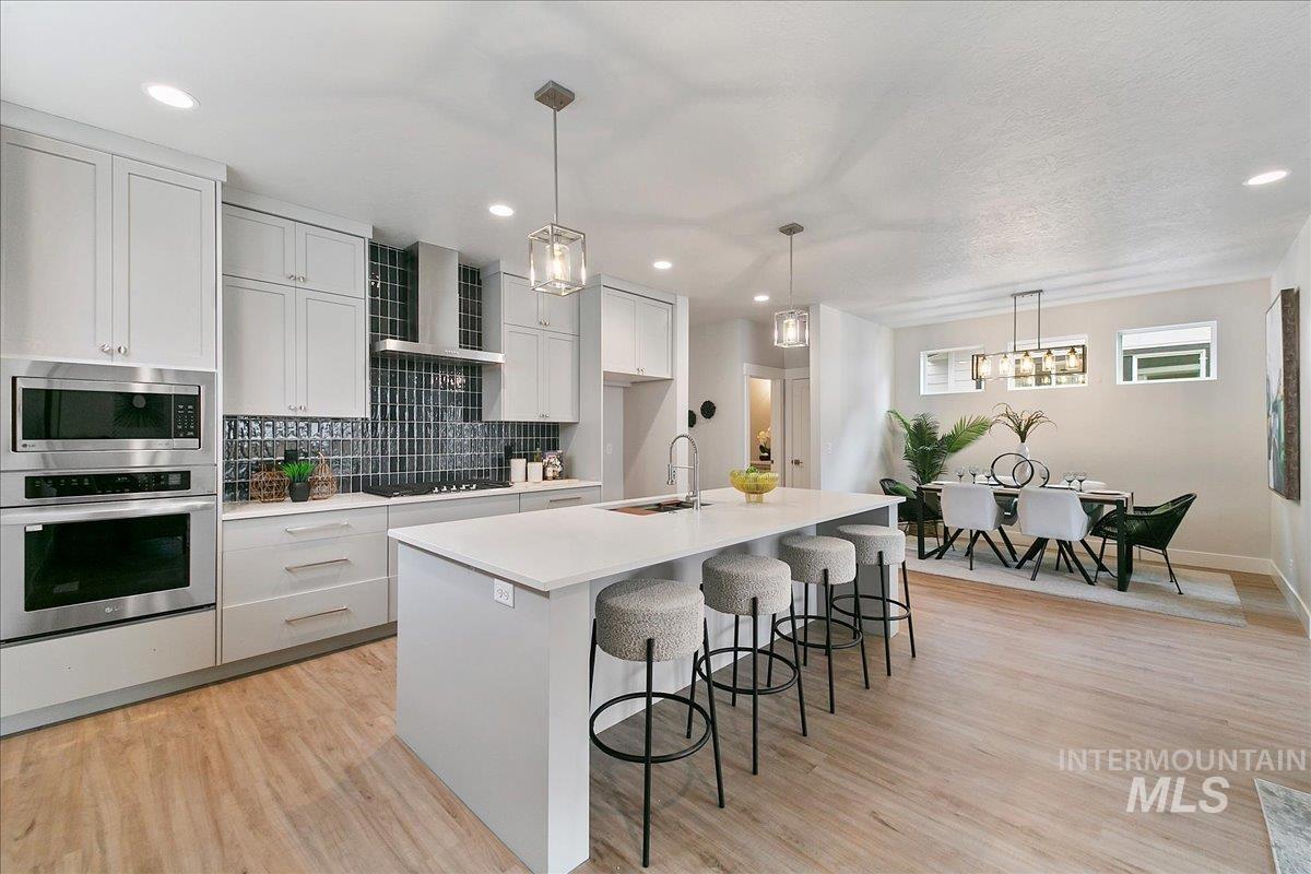 Kitchen featuring stainless steel appliances, backsplash, a breakfast bar area, decorative light fixtures, and wall chimney range hood