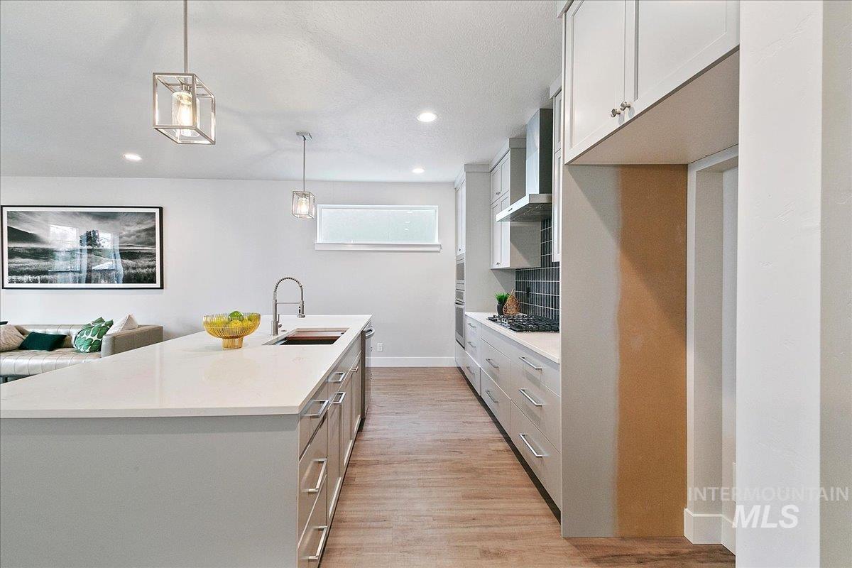 Kitchen with white cabinetry, hanging light fixtures, light wood-style flooring, wall chimney range hood, and recessed lighting