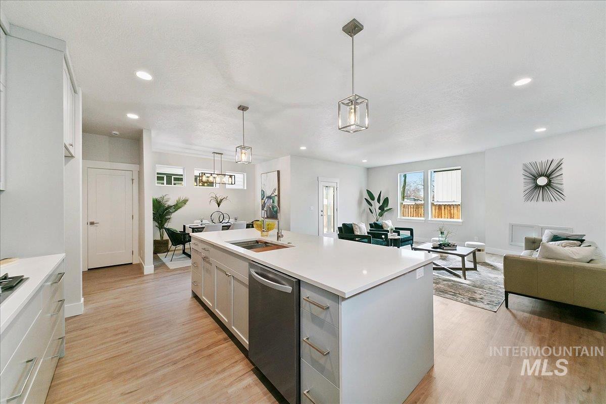 Kitchen featuring open floor plan, stainless steel dishwasher, light wood-type flooring, a center island with sink, and hanging light fixtures