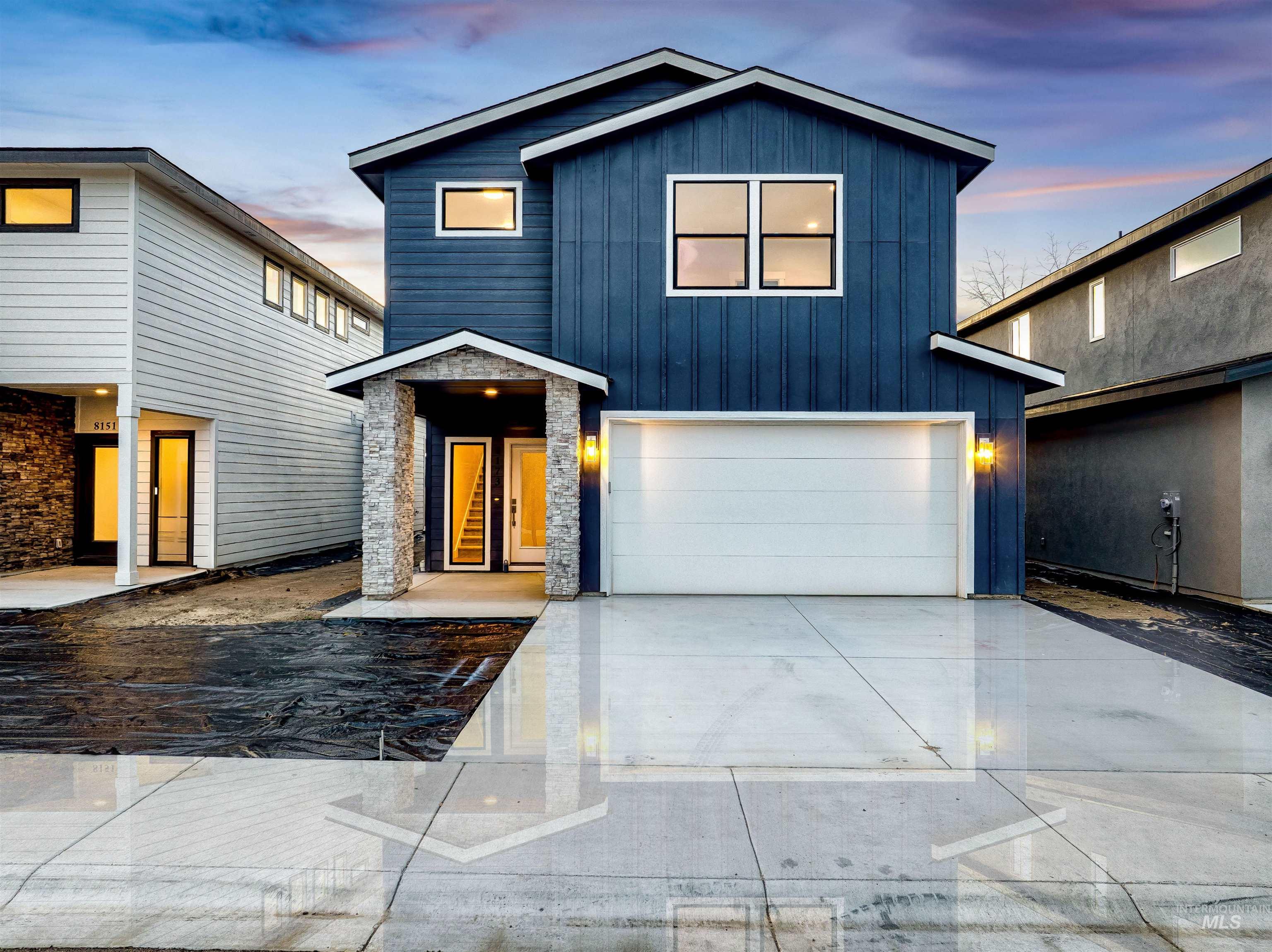 Modern home featuring board and batten siding, driveway, an attached garage, and stone siding
