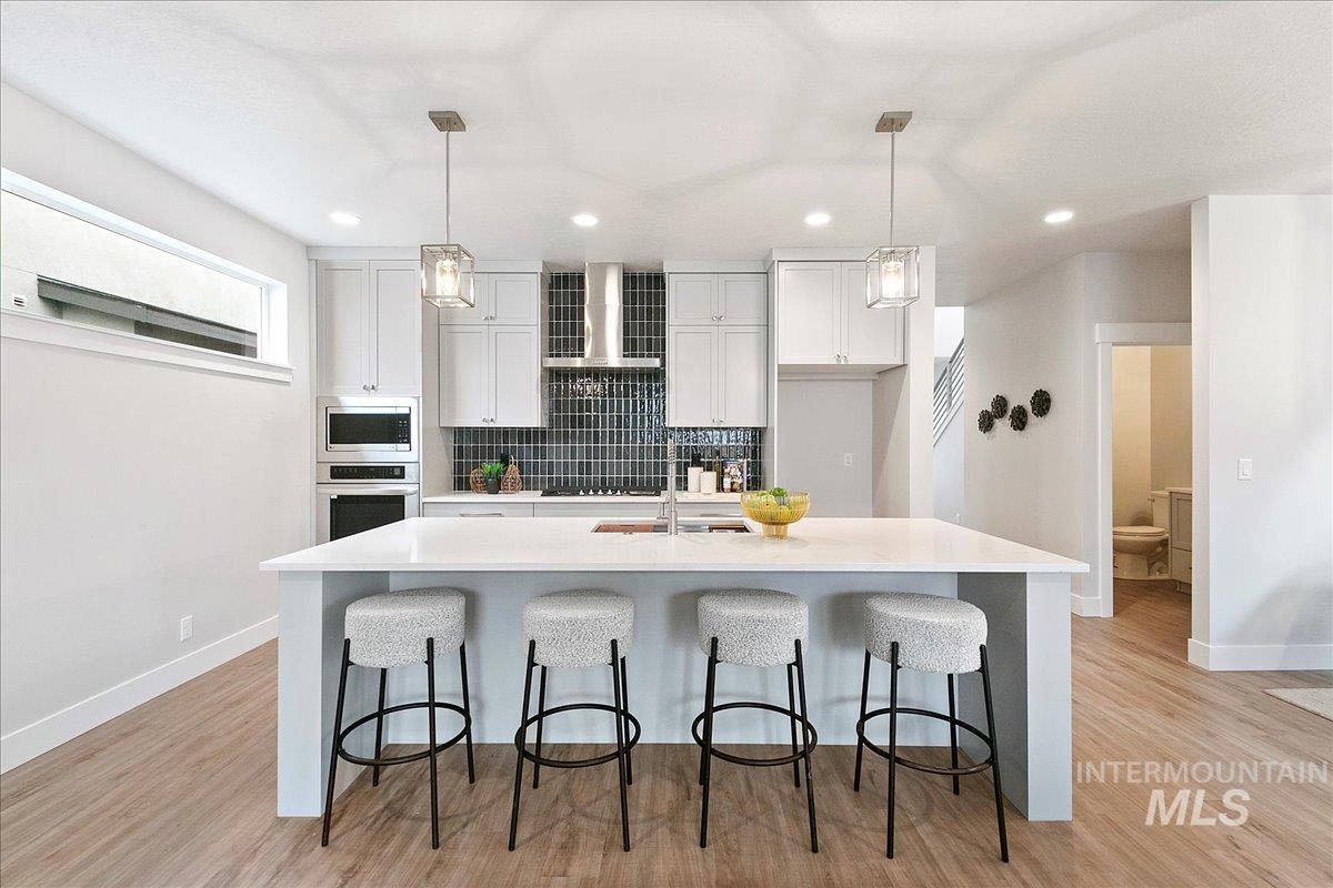 Kitchen with a kitchen bar, tasteful backsplash, a kitchen island with sink, light wood-type flooring, and recessed lighting