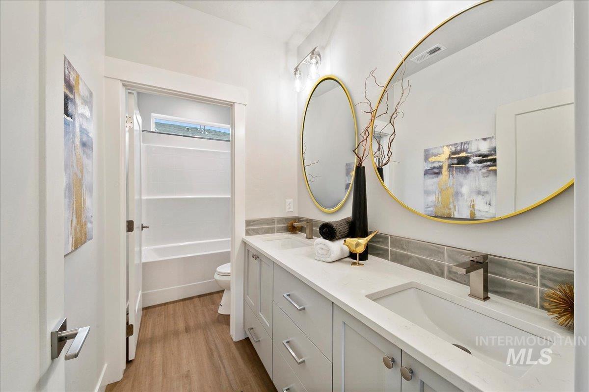 Bathroom featuring double vanity, light wood-style flooring, and washtub / shower combination