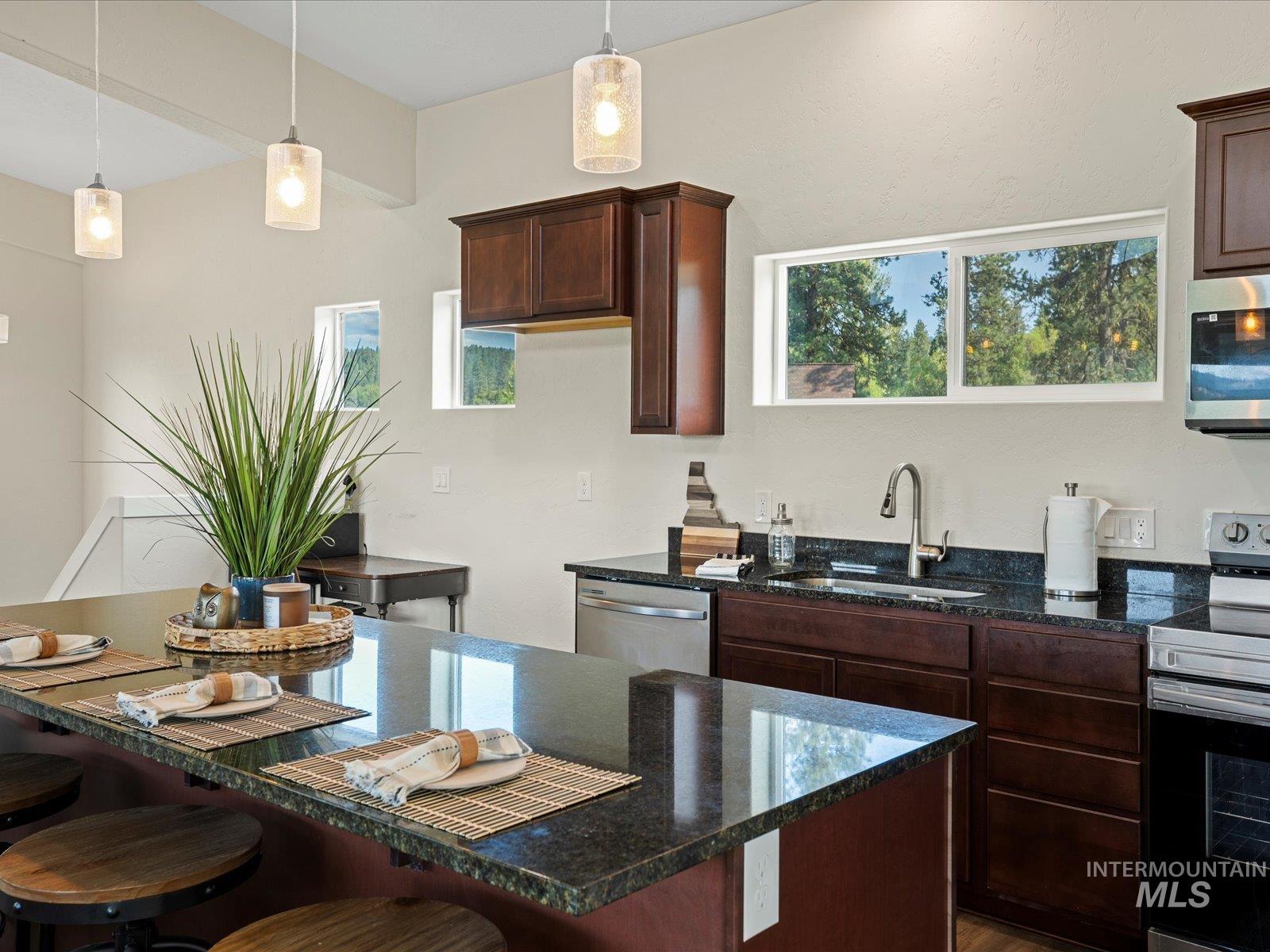 Kitchen featuring appliances with stainless steel finishes, a kitchen bar, dark stone counters, and decorative light fixtures