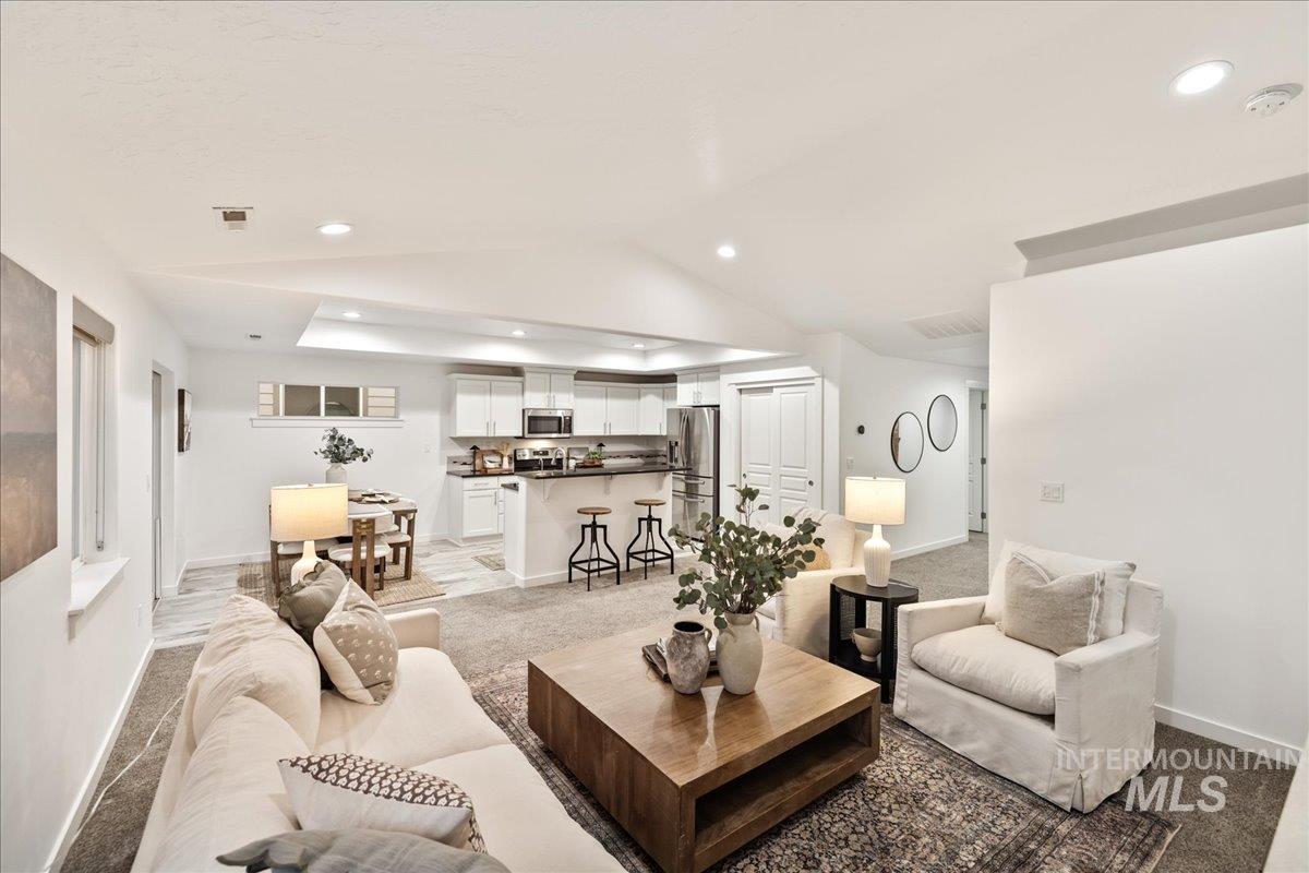 Living area with light colored carpet, lofted ceiling, a raised ceiling, and recessed lighting