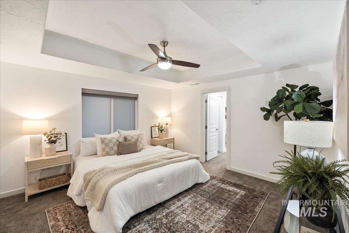 Bedroom featuring a raised ceiling, dark carpet, and a ceiling fan