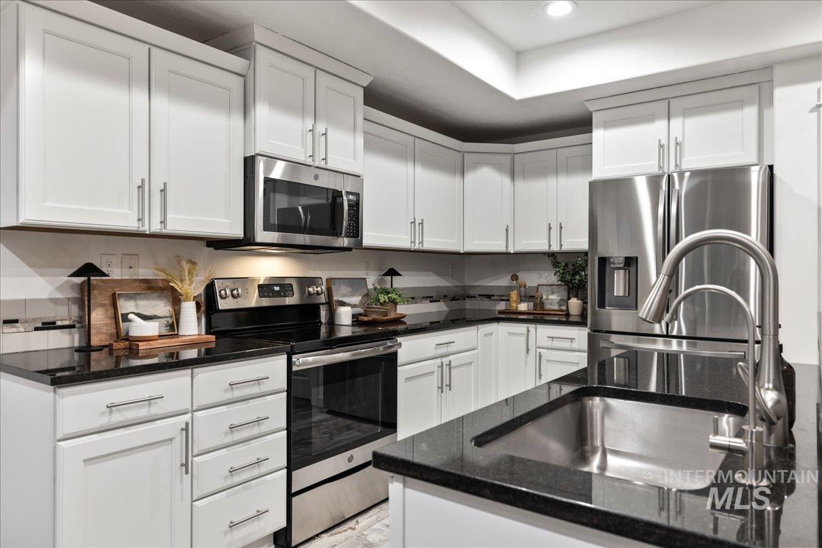 Kitchen with appliances with stainless steel finishes, white cabinetry, dark stone countertops, and recessed lighting