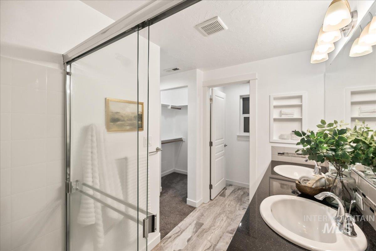 Bathroom featuring double vanity, a shower stall, a spacious closet, and light wood finished floors