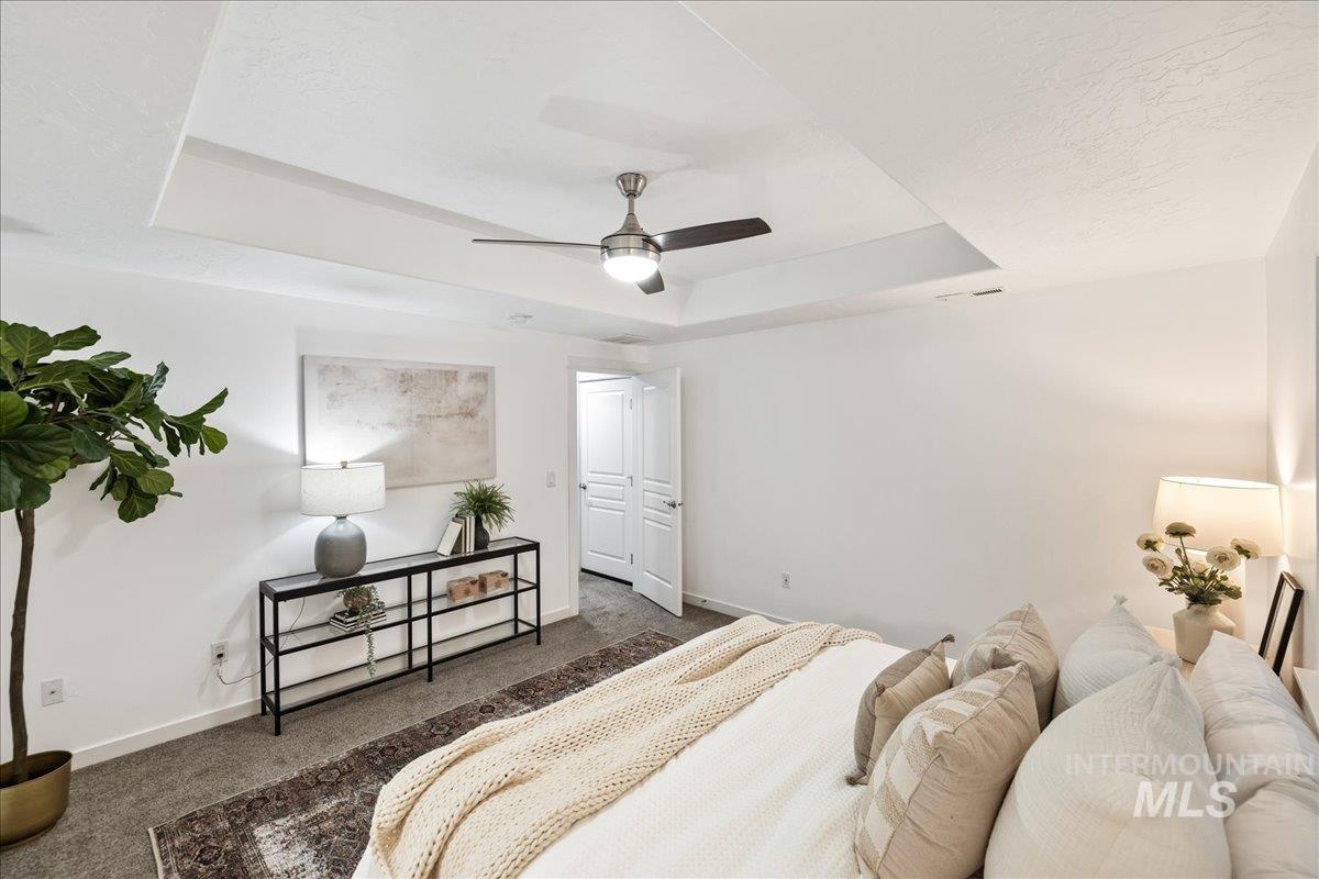 Carpeted bedroom featuring a tray ceiling and ceiling fan