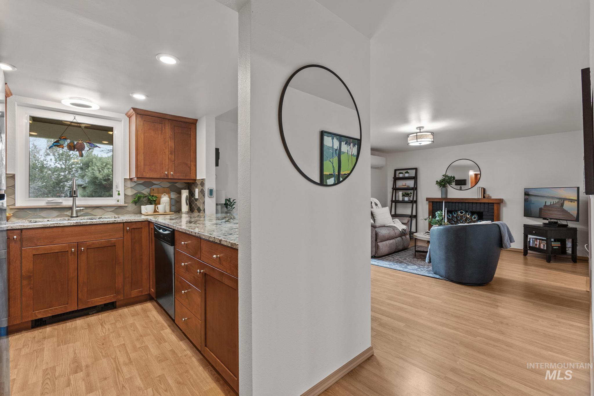Kitchen featuring wood finish cabinetry, light wood-type flooring, light stone countertops, open floor plan, and backsplash