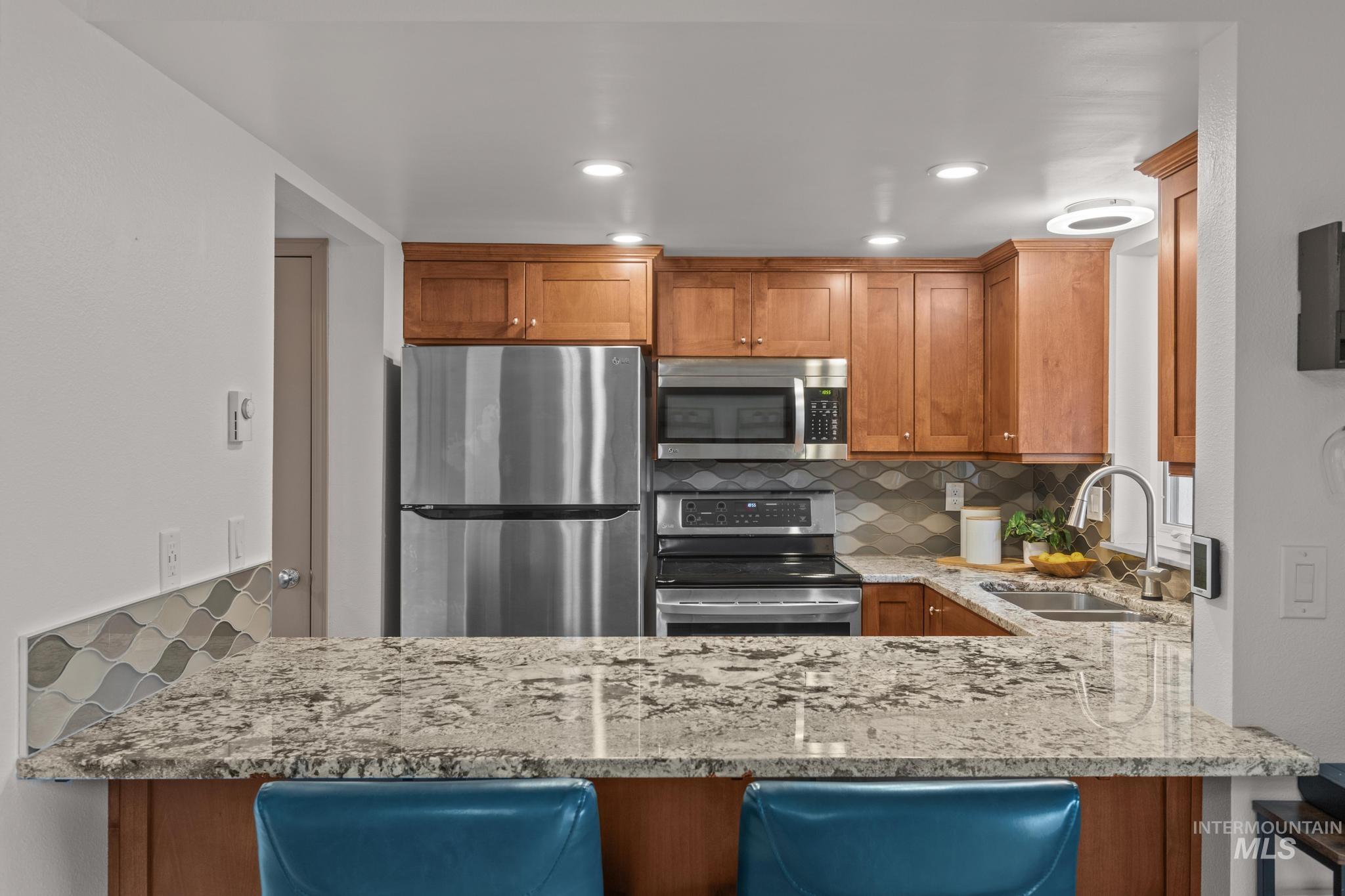 Kitchen with tasteful backsplash, light stone countertops, wood finish cabinets, stainless steel appliances, and recessed lighting