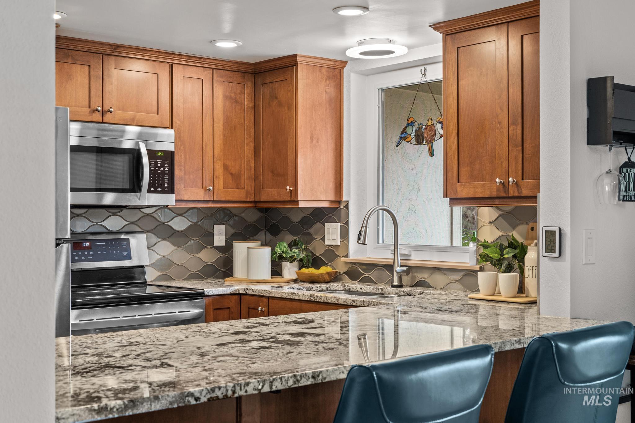 Kitchen with wood finish cabinets, stainless steel appliances, light stone counters, and backsplash