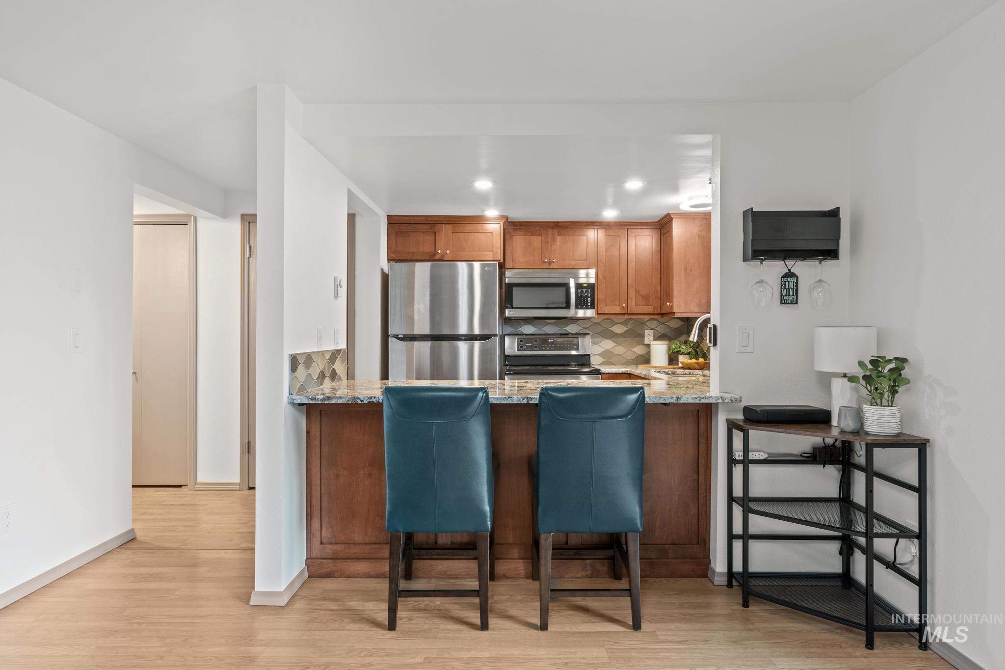 Kitchen featuring light stone countertops, wood finish cabinets, stainless steel appliances, a peninsula, and light wood-style floors