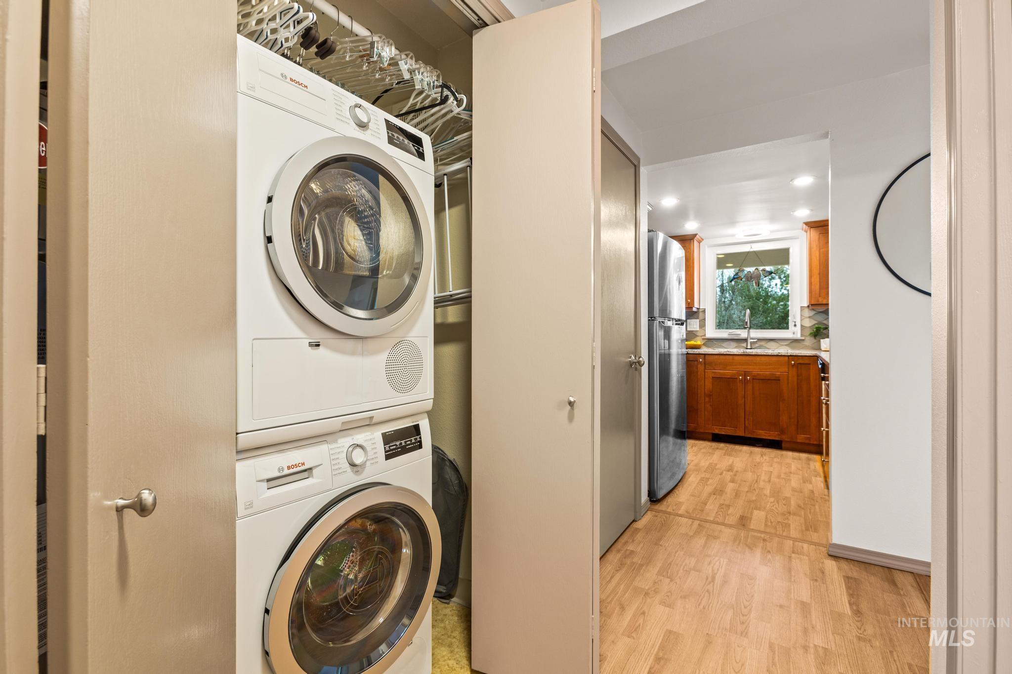 Laundry area featuring light wood-style floors, stacked washing machine and dryer, and recessed lighting