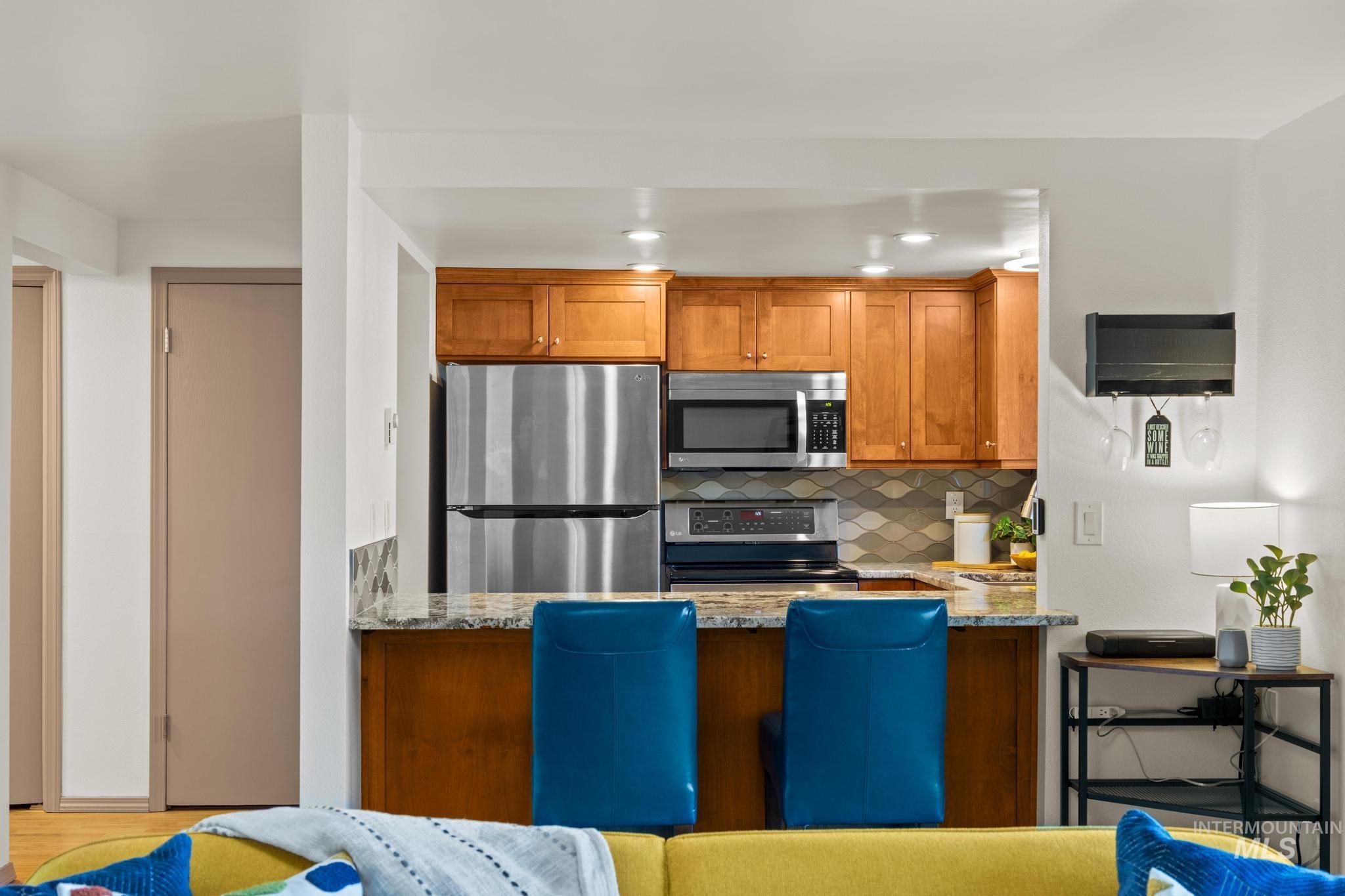 Kitchen with light stone counters, wood finish cabinets, stainless steel appliances, decorative backsplash, and recessed lighting