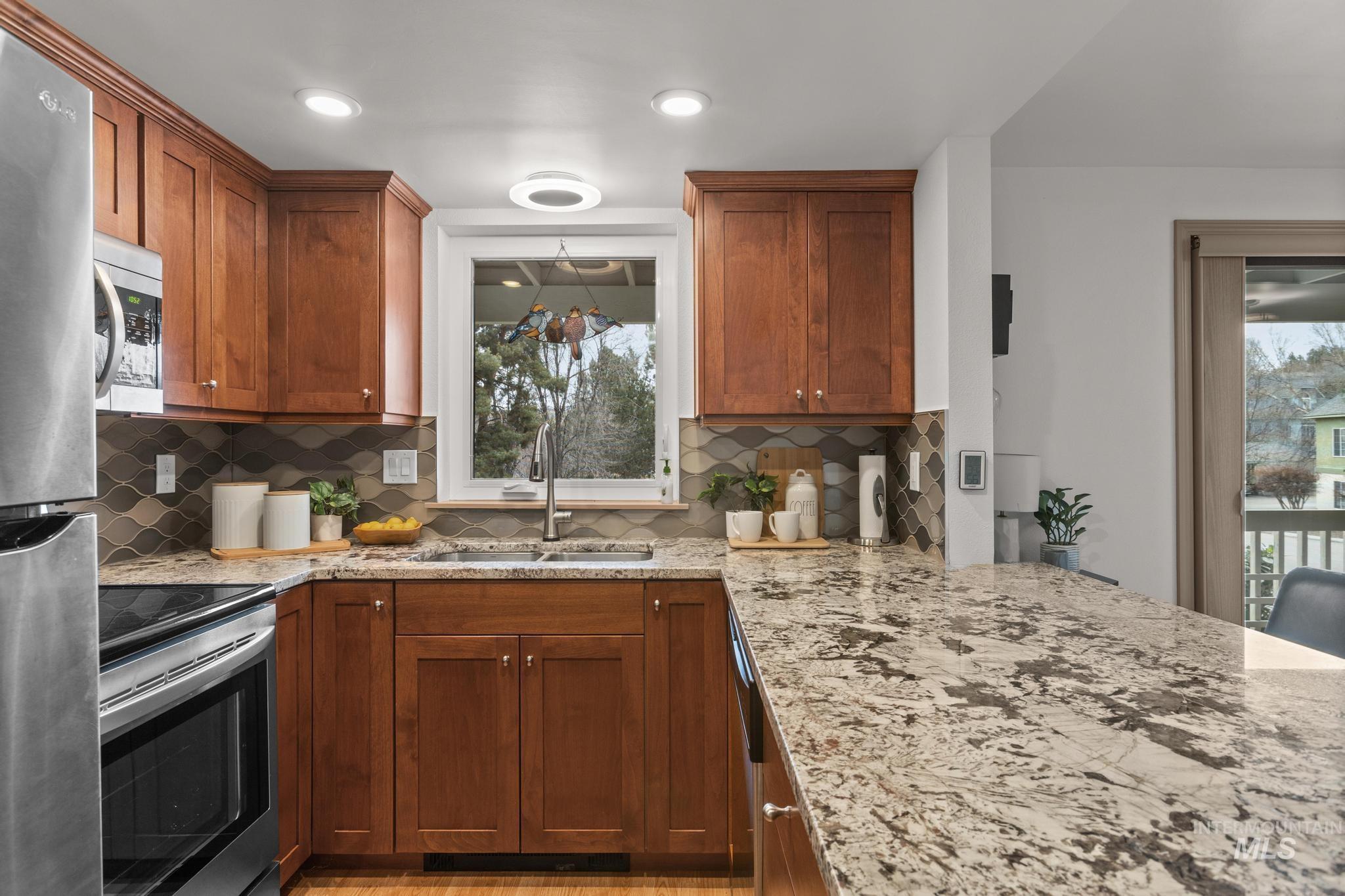 Kitchen with wood finish cabinetry, stainless steel appliances, light stone countertops, a peninsula, and tasteful backsplash