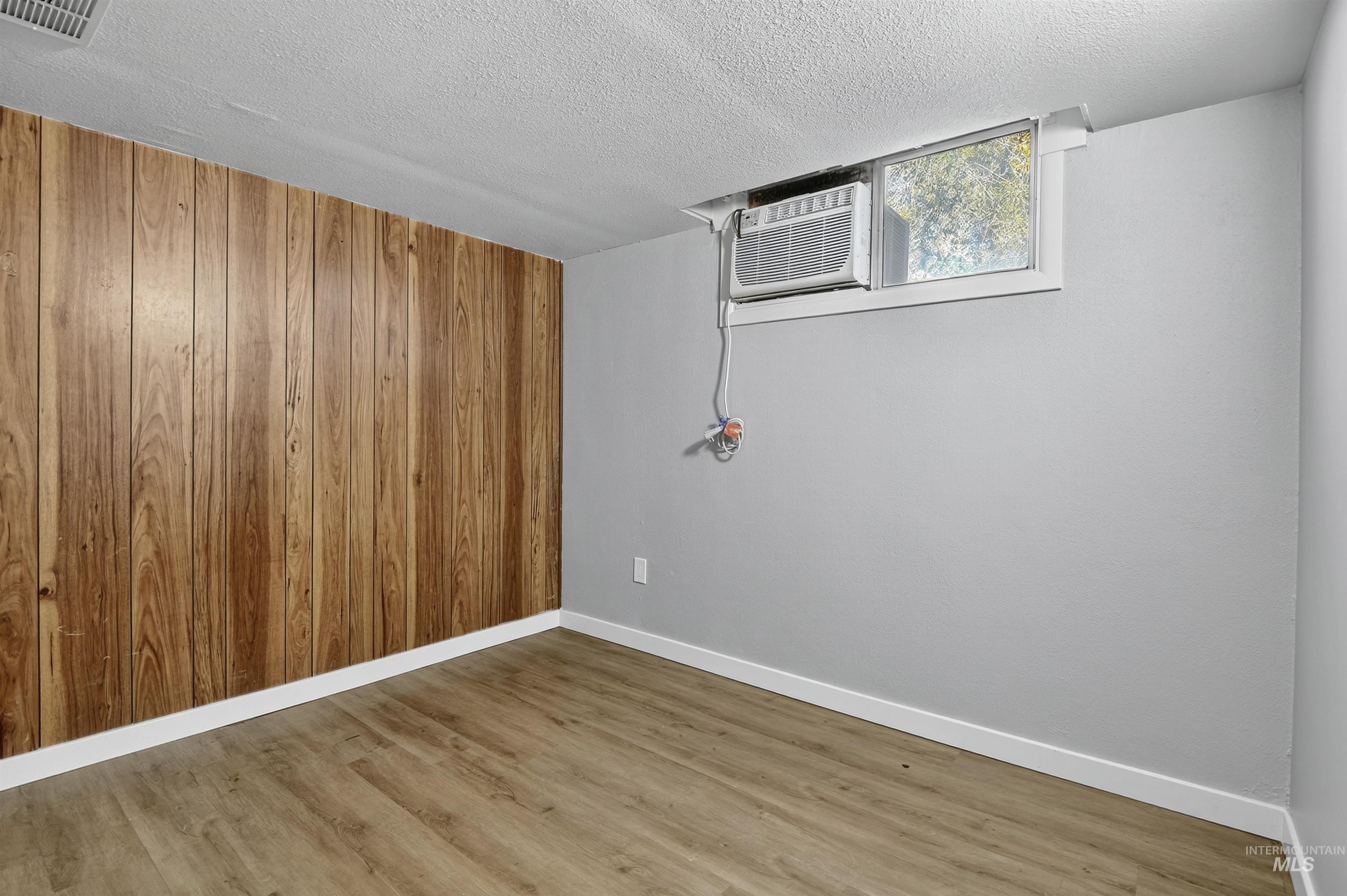 Empty room with wood finished floors, wooden walls, and a textured ceiling