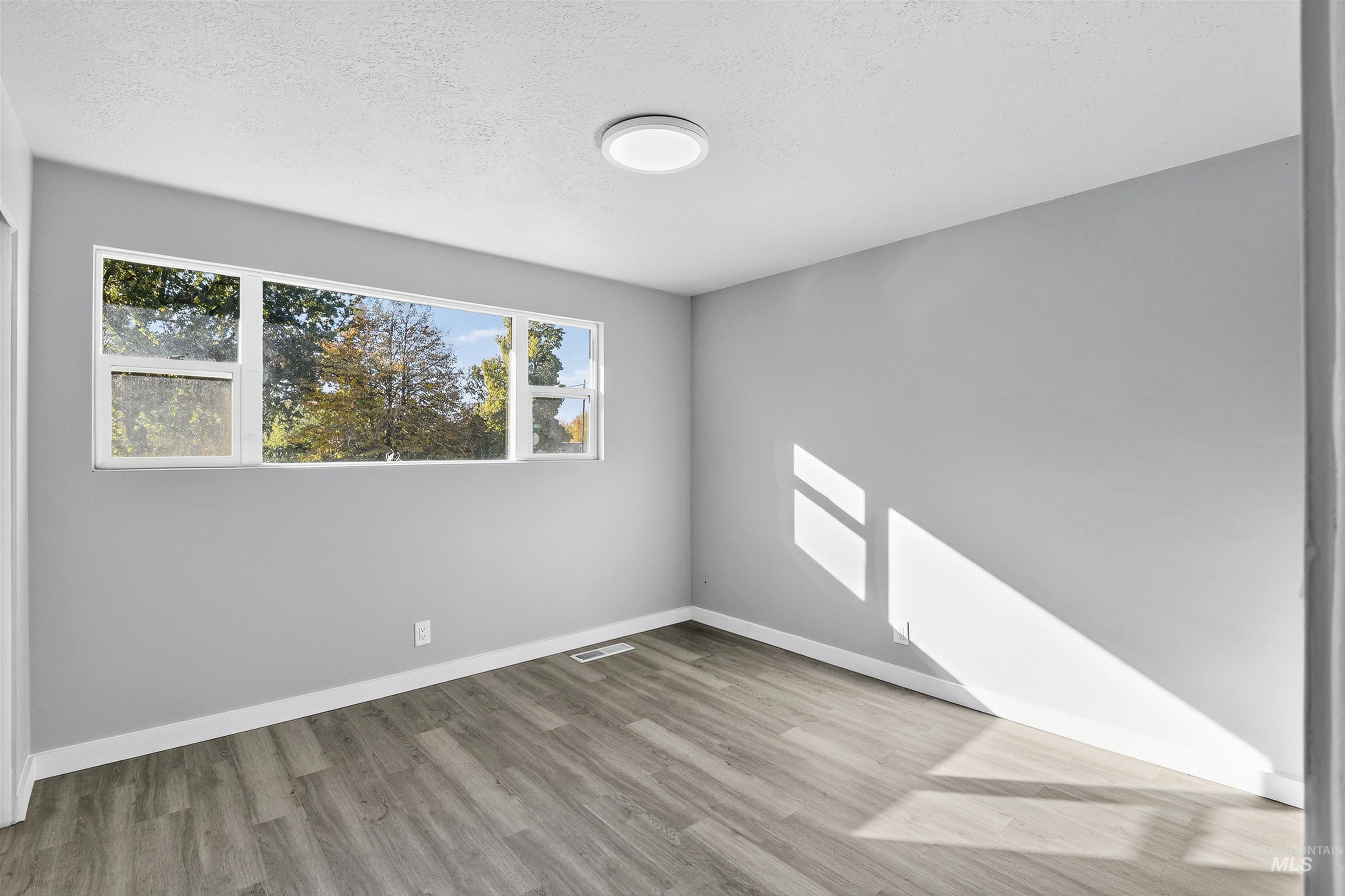 Unfurnished room featuring healthy amount of natural light, light wood-style flooring, and a textured ceiling