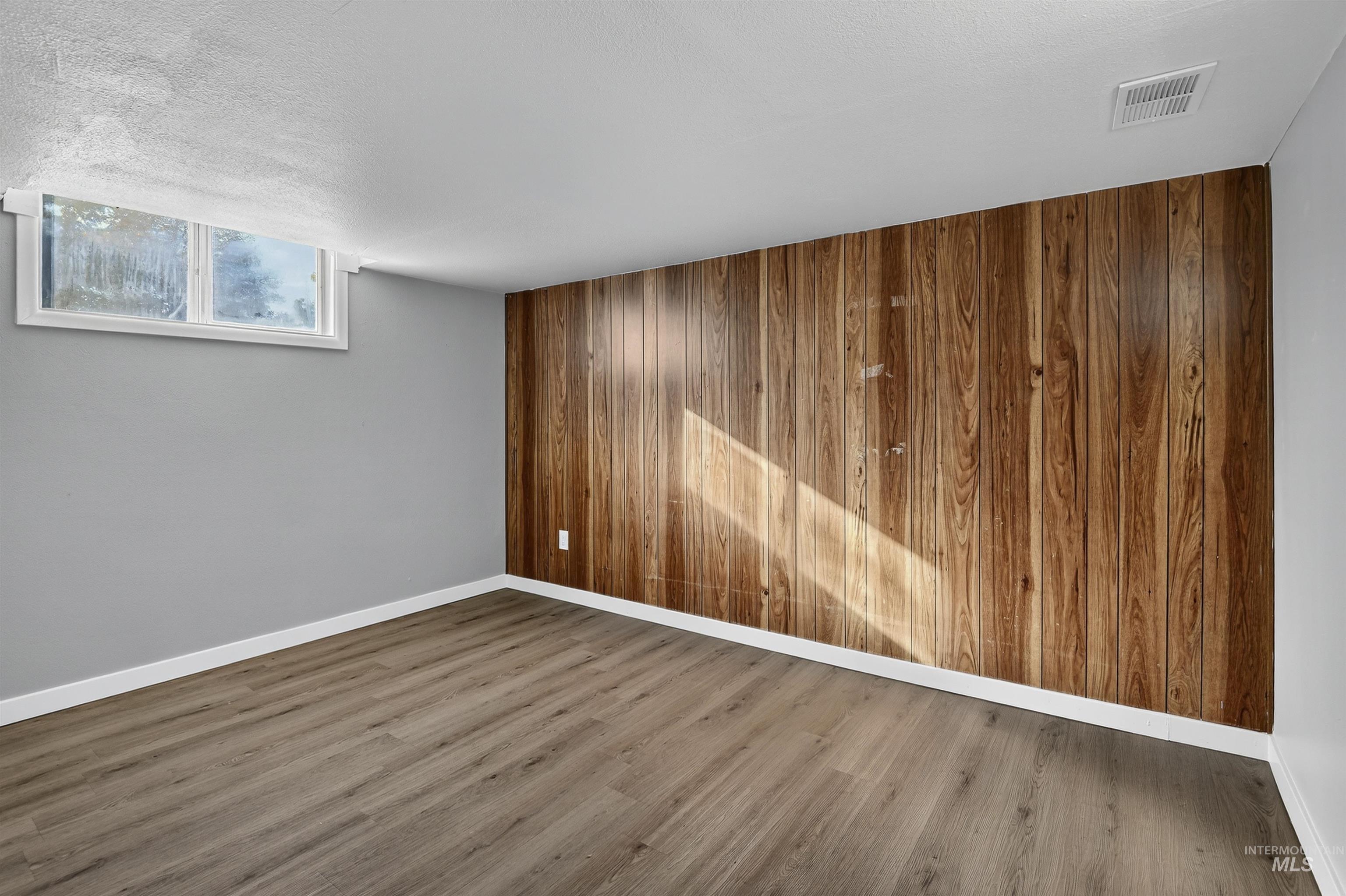 Spare room featuring wooden walls, wood finished floors, and a textured ceiling