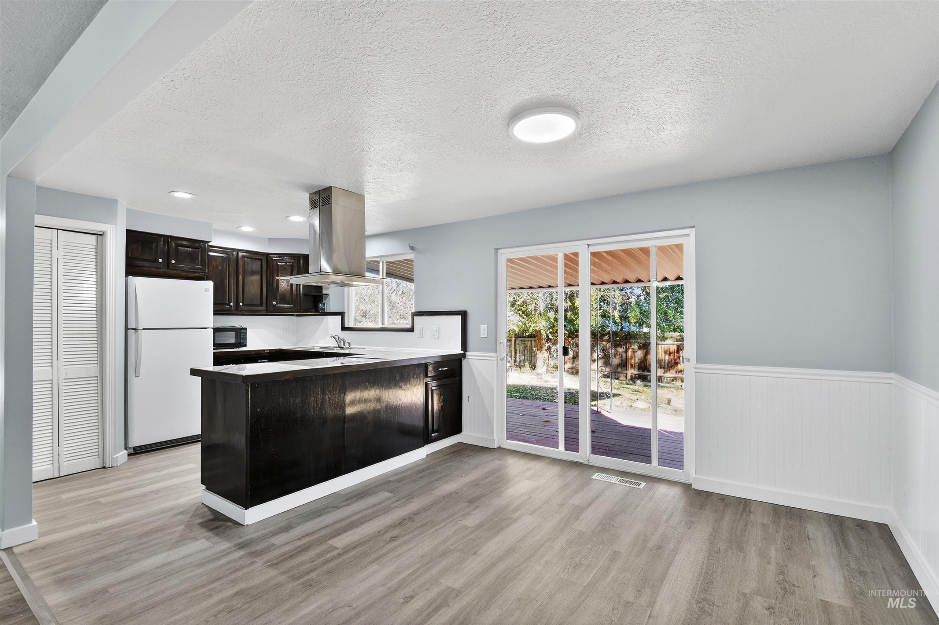 Kitchen featuring a peninsula, freestanding refrigerator, dark brown cabinets, a textured ceiling, and light wood-style floors
