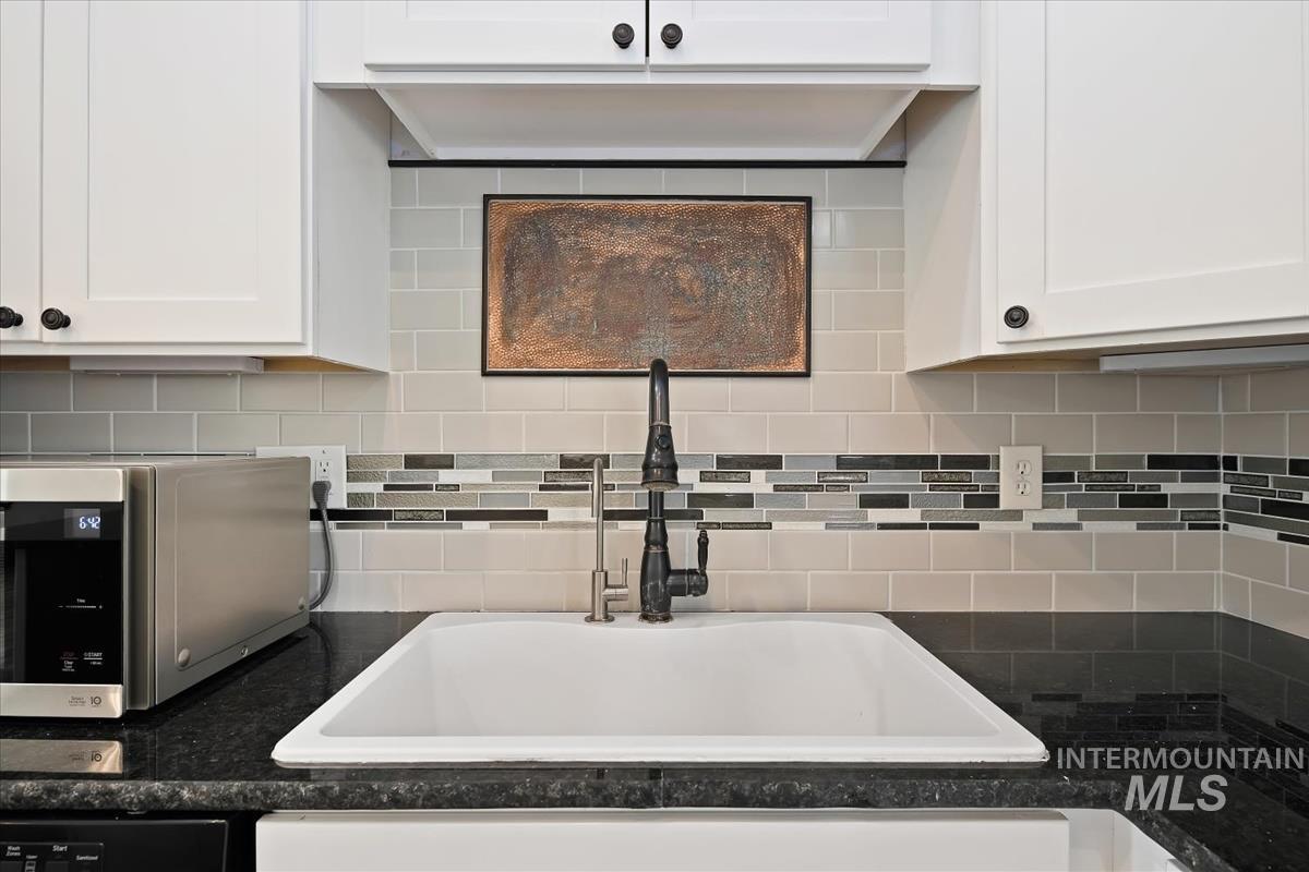 Kitchen featuring white cabinets, stainless steel microwave, and backsplash