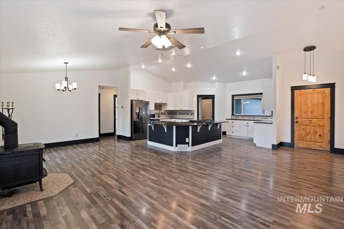 Living room featuring a wood stove, a ceiling fan, dark wood finished floors, vaulted ceiling, and hanging lights