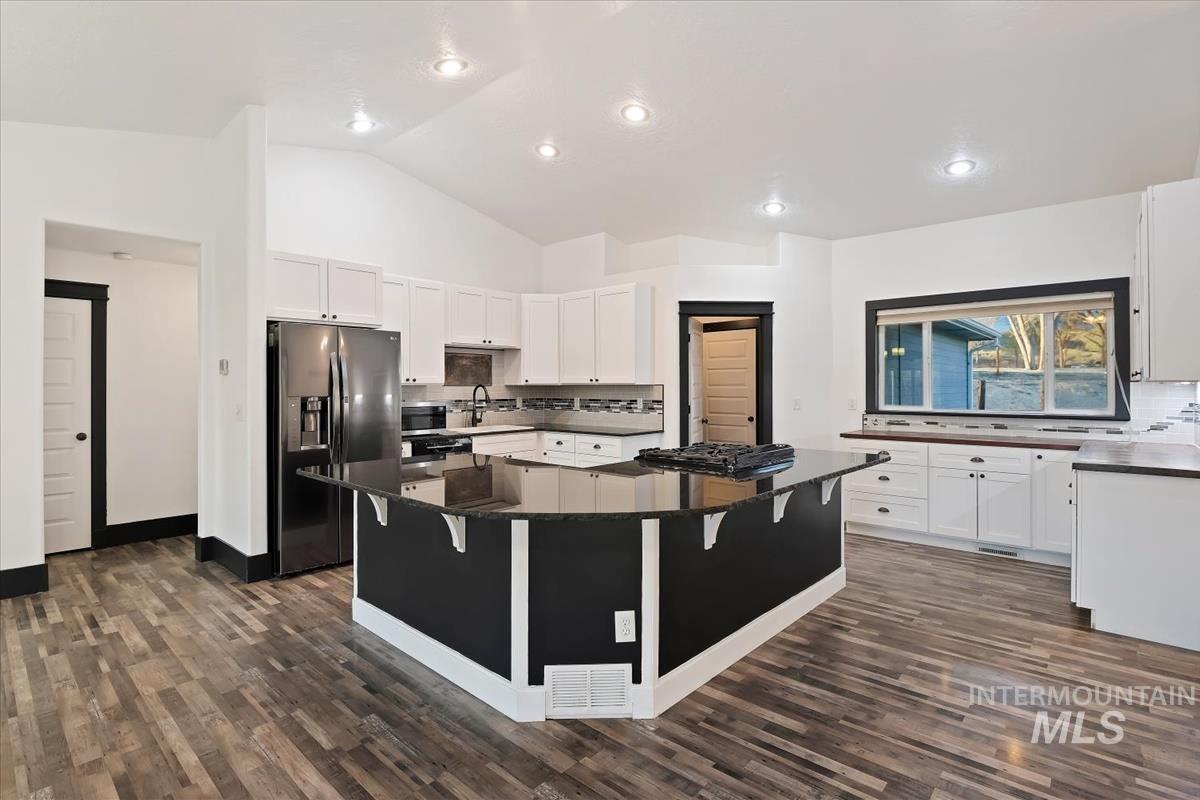 Kitchen with tasteful backsplash, refrigerator with ice dispenser, dark stone counters, a kitchen island, and a breakfast bar area