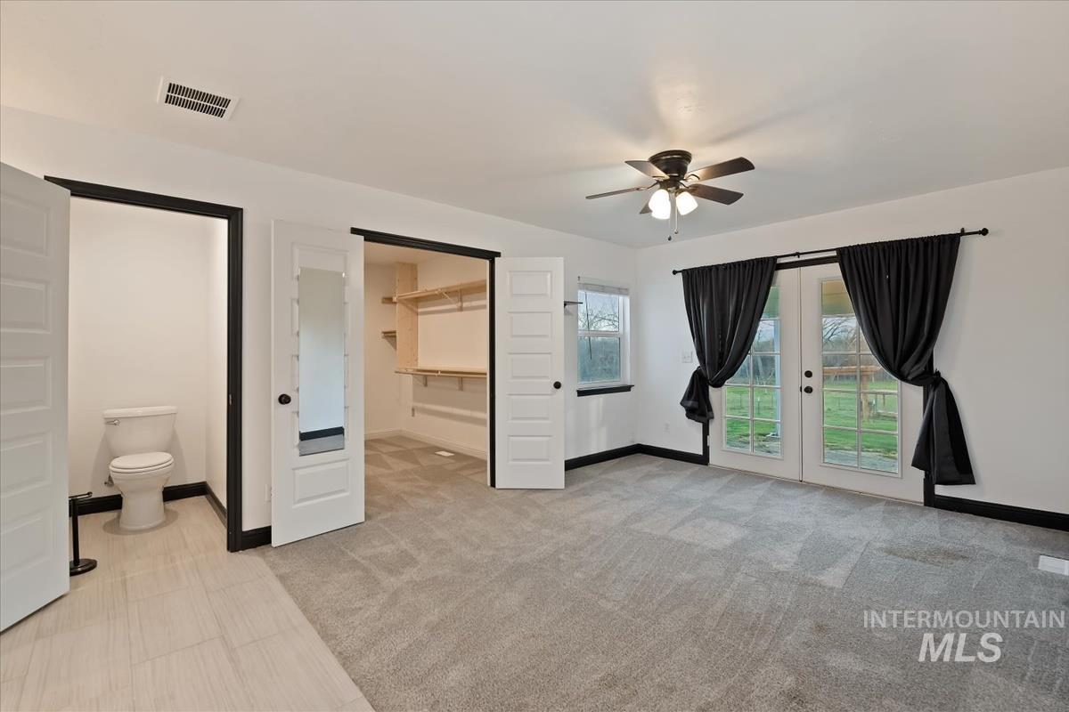 Unfurnished bedroom featuring french doors, a spacious closet, access to outside, ceiling fan, and ensuite bathroom