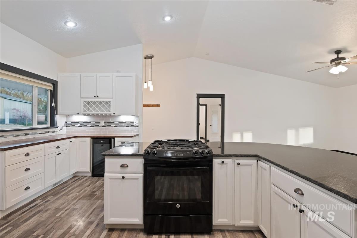 Kitchen featuring black range with gas stovetop, white cabinets, dark wood-type flooring, tasteful backsplash, and vaulted ceiling