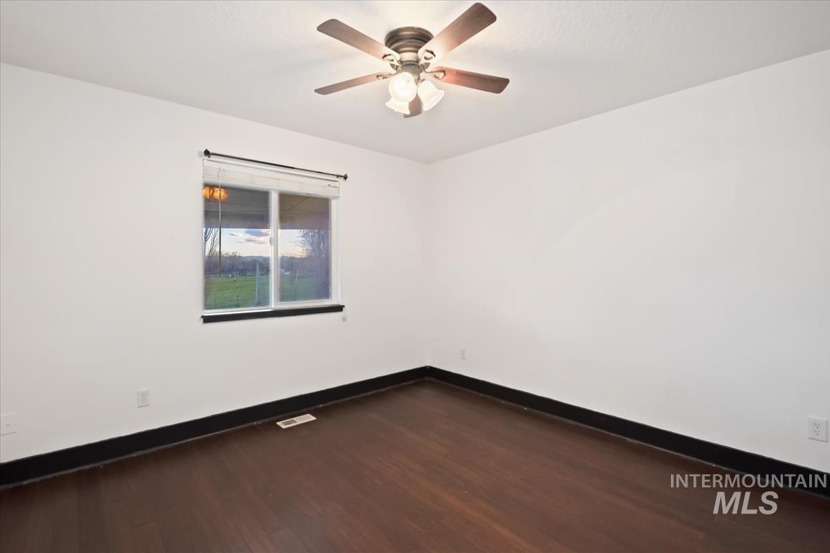Empty room with dark wood-style floors and a ceiling fan