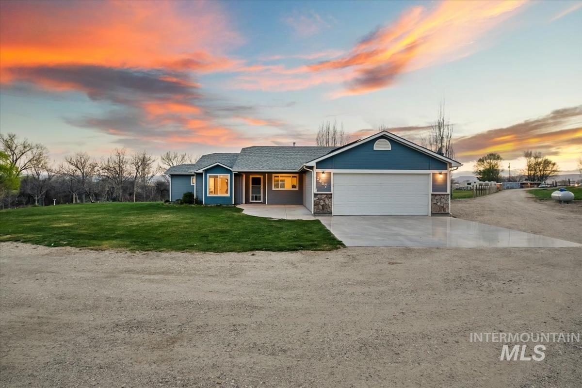 Ranch-style home featuring concrete driveway, an attached garage, a lawn, and stone siding