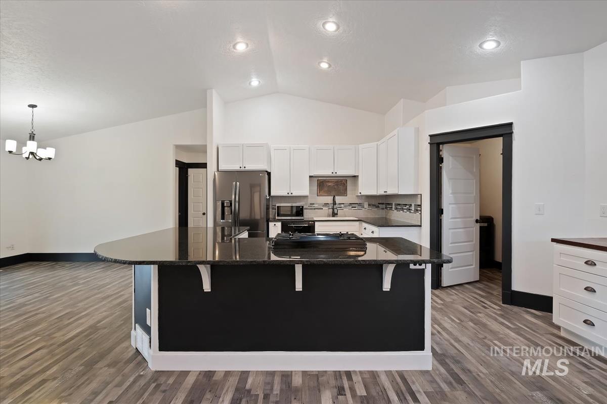 Kitchen featuring white cabinets, a breakfast bar area, dark stone countertops, stainless steel appliances, and lofted ceiling