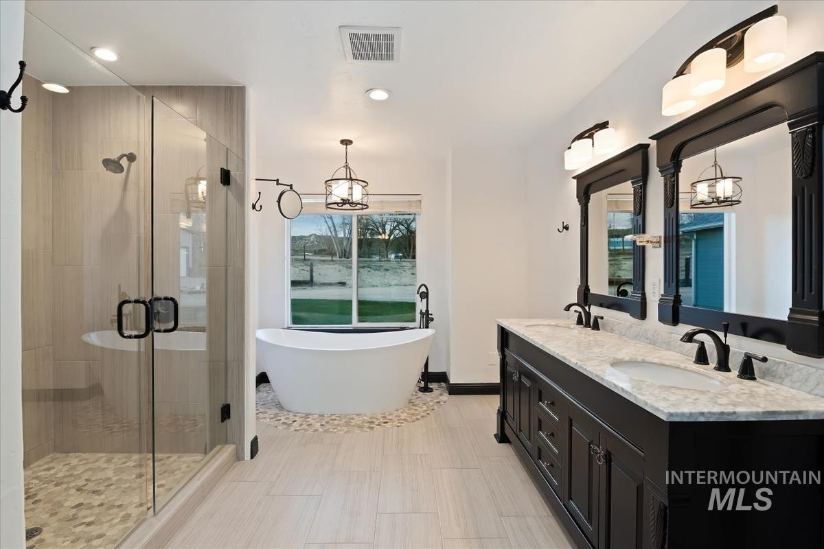 Full bathroom with double vanity, a stall shower, suspended lighting, and a soaking tub